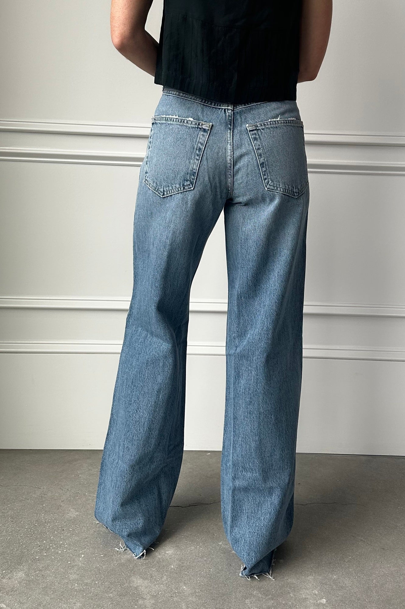 Person wearing blue jeans and a black top against a gray wall.