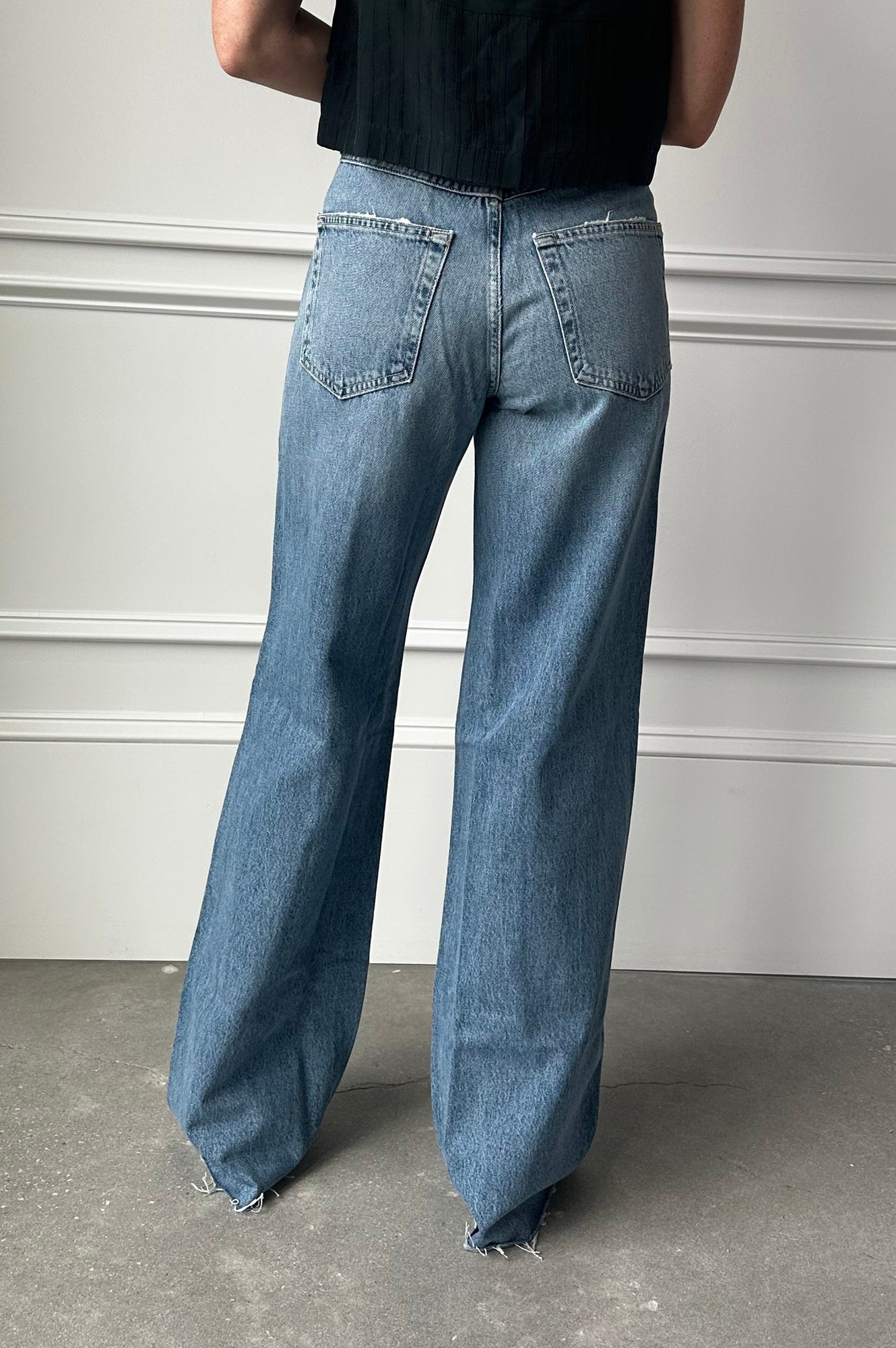 Person wearing blue jeans and a black top against a neutral background