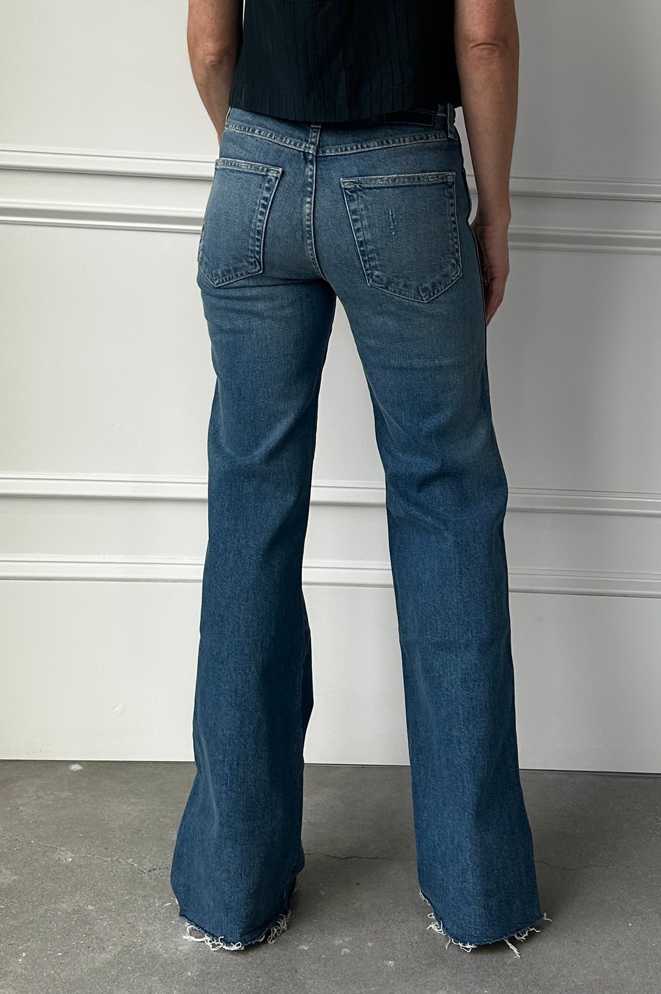 Person wearing blue flared jeans standing against a white wall.