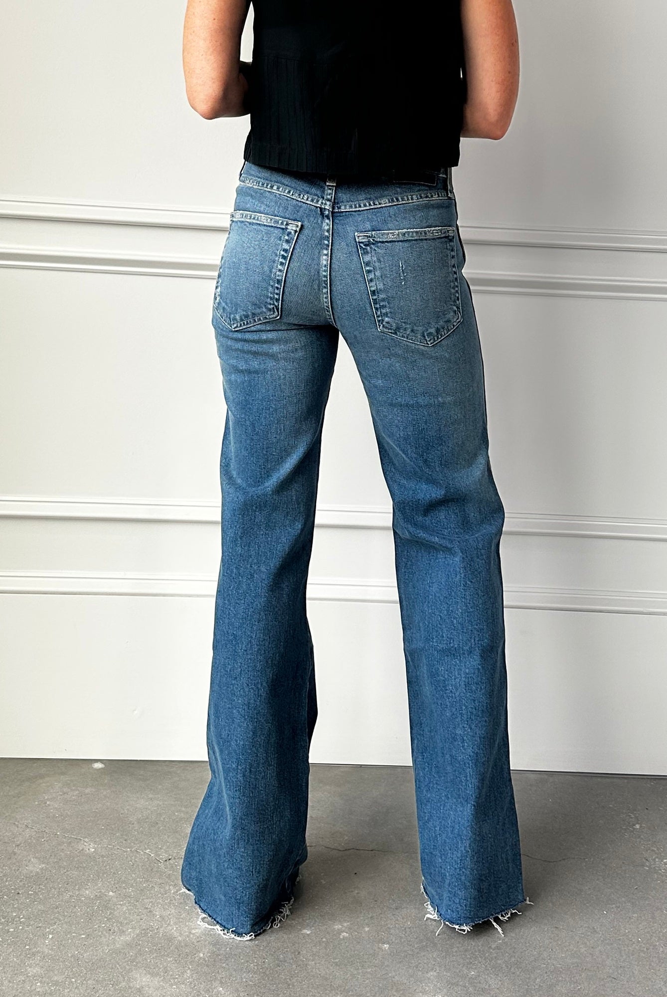 Person wearing blue flared jeans from behind against a plain background