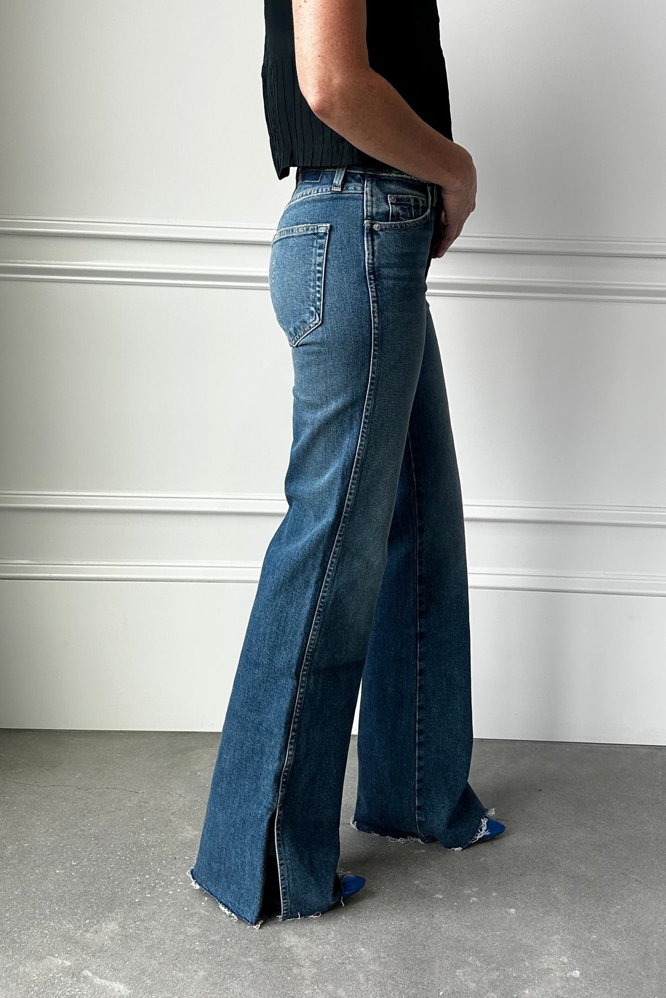Person wearing blue flared jeans against a white wall.