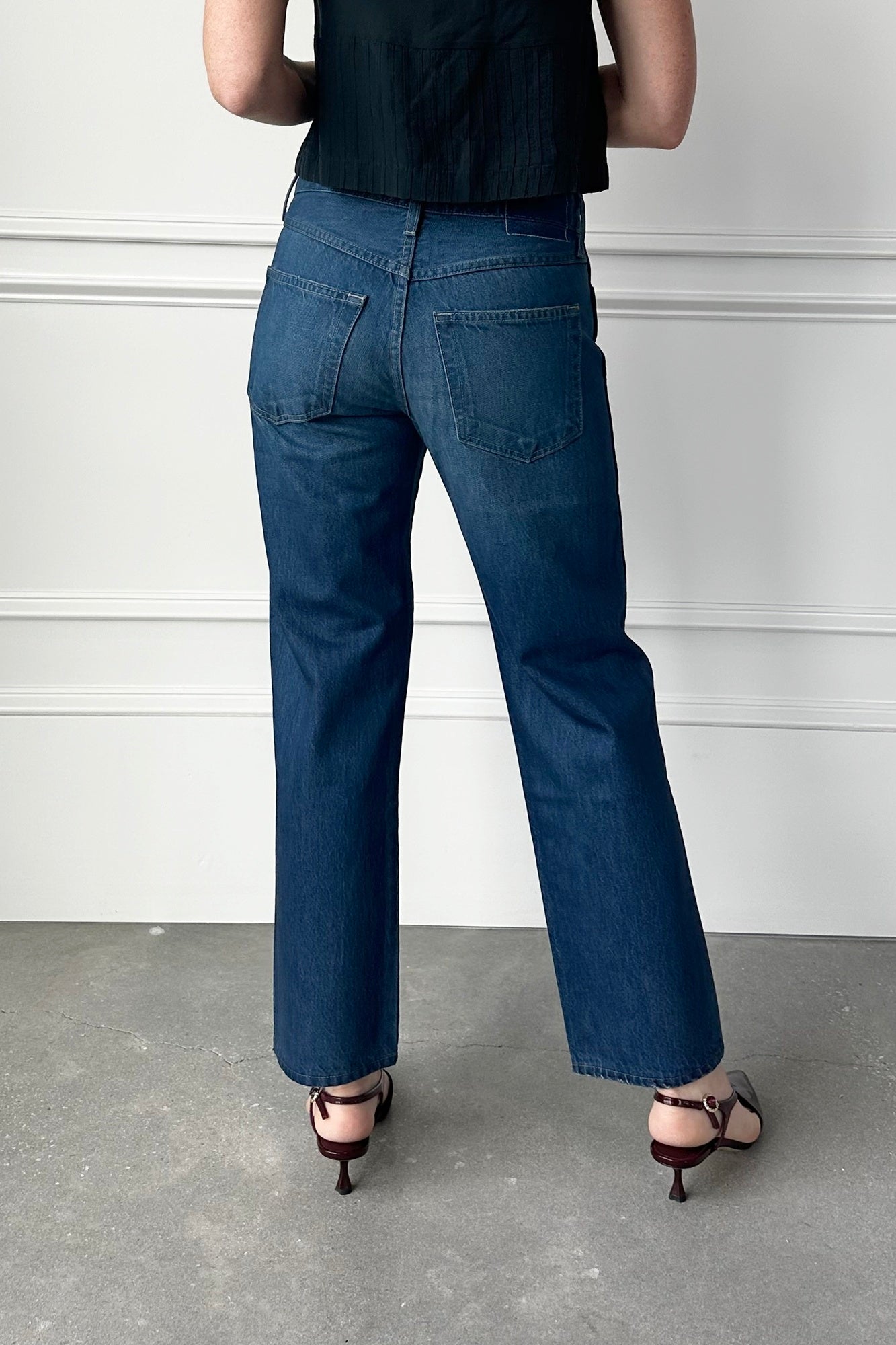 Person wearing blue jeans and a black top against a white wall.