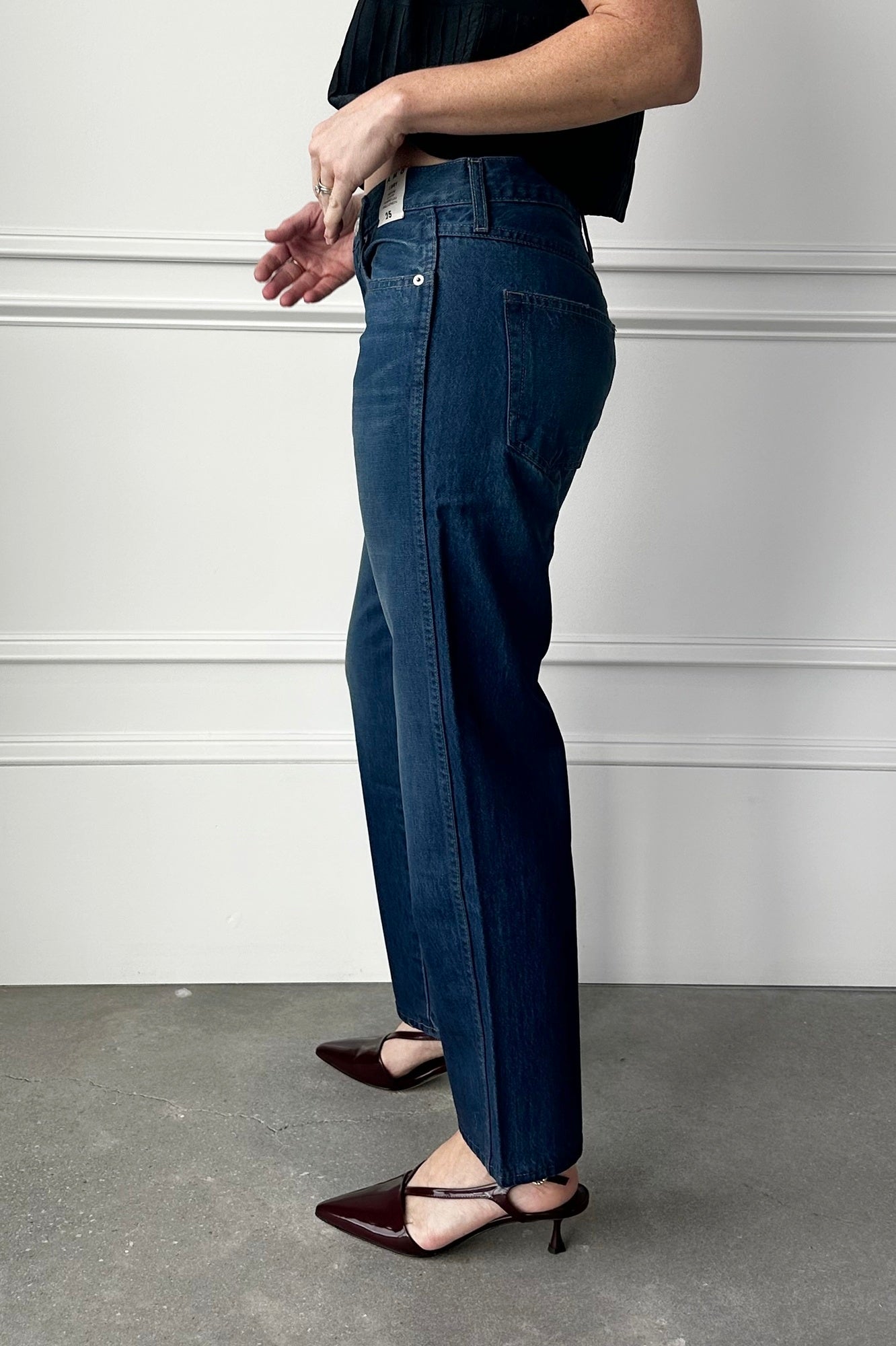 Person wearing dark blue jeans and black shoes on a plain background