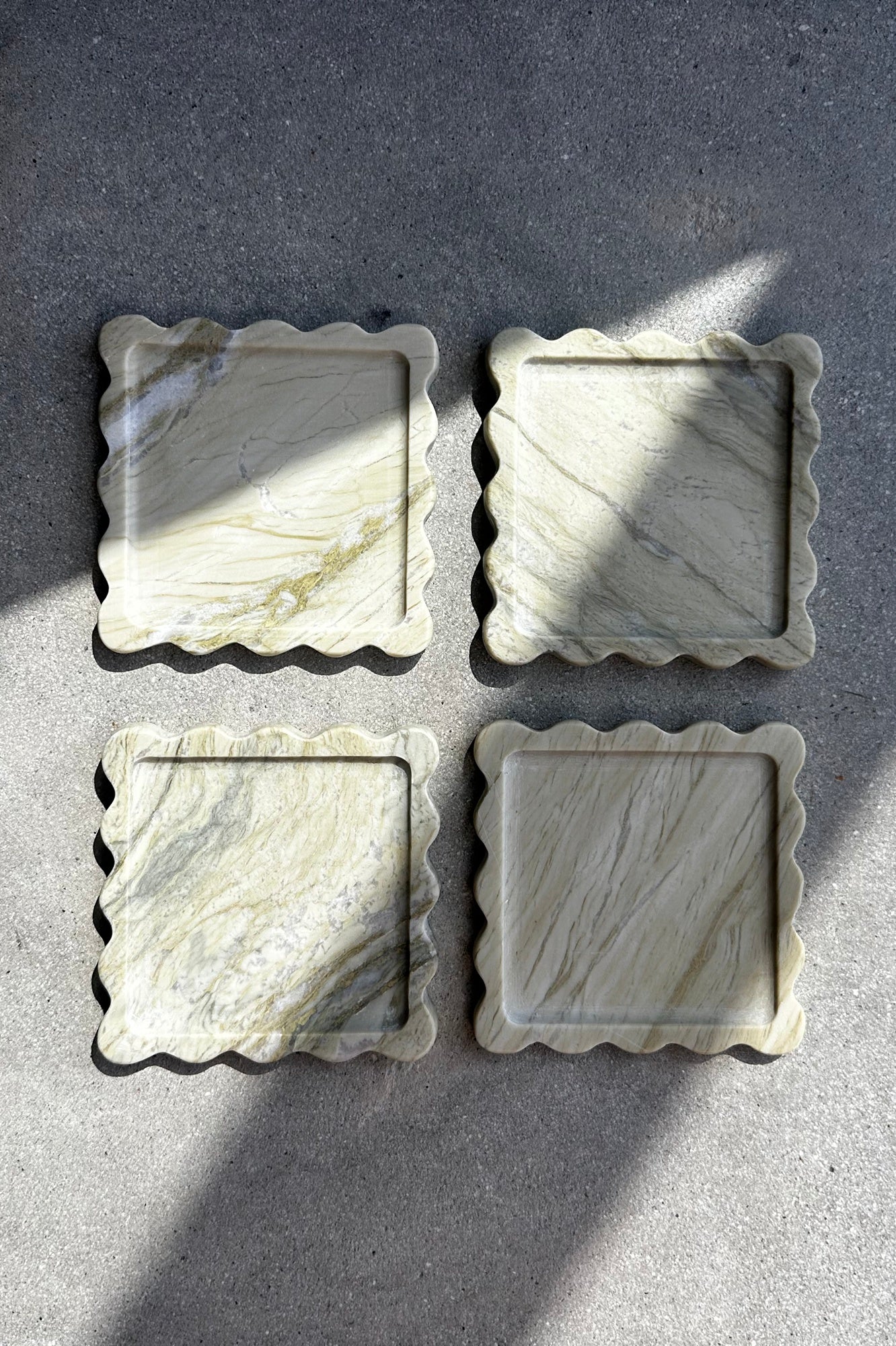 Four square marble coasters with decorative edges on a gray surface