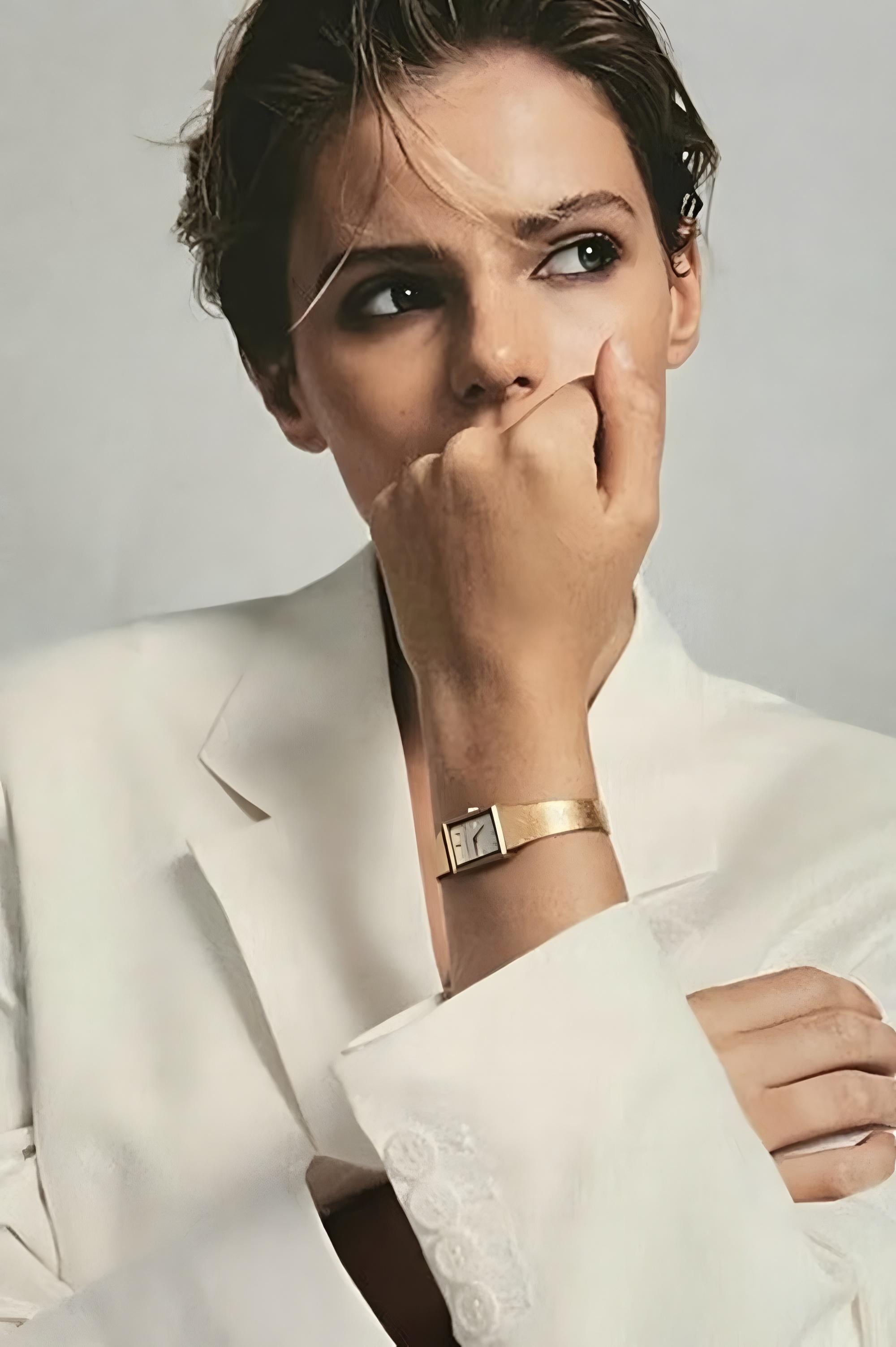 Woman in a white suit with a gold watch on her wrist, posing thoughtfully.