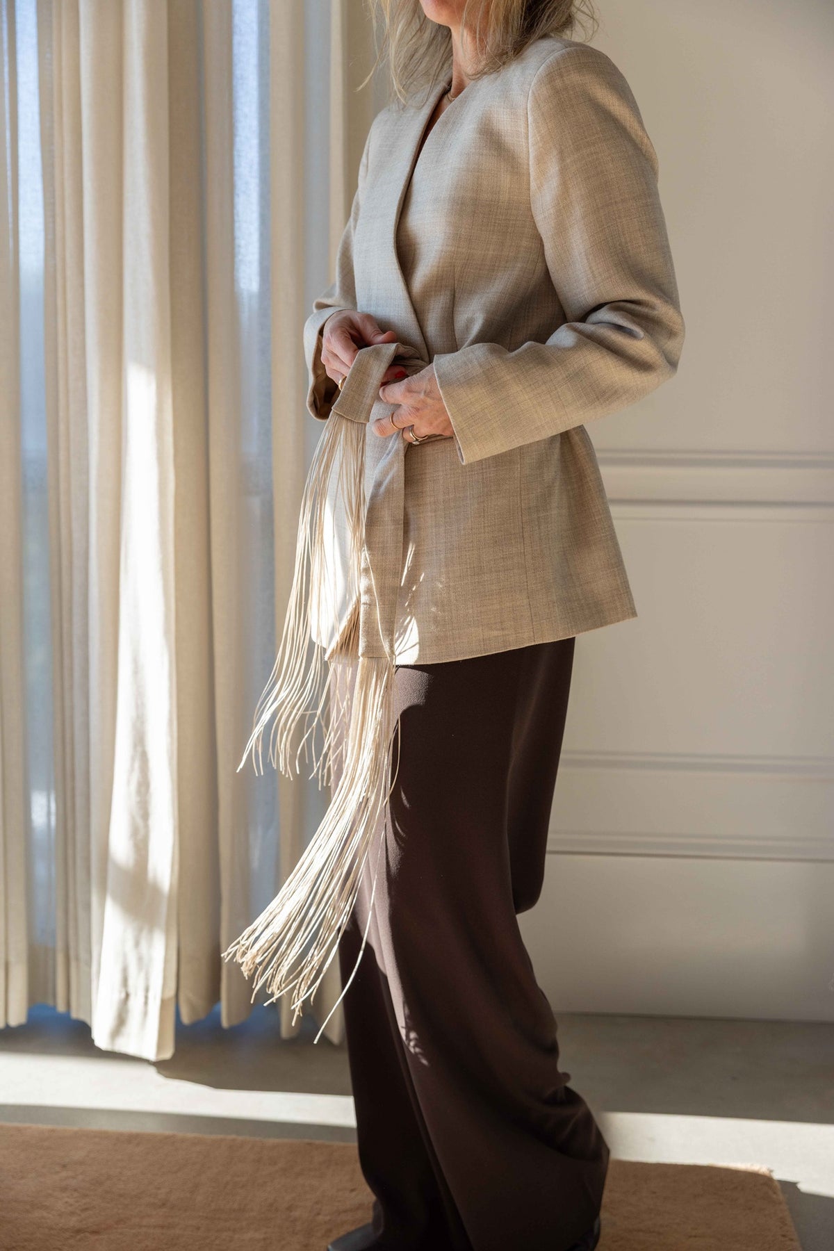by Malene Birger Emma Blazer in grey brown melange, side view showing the wrap front and long fringed tie belt over dark trousers