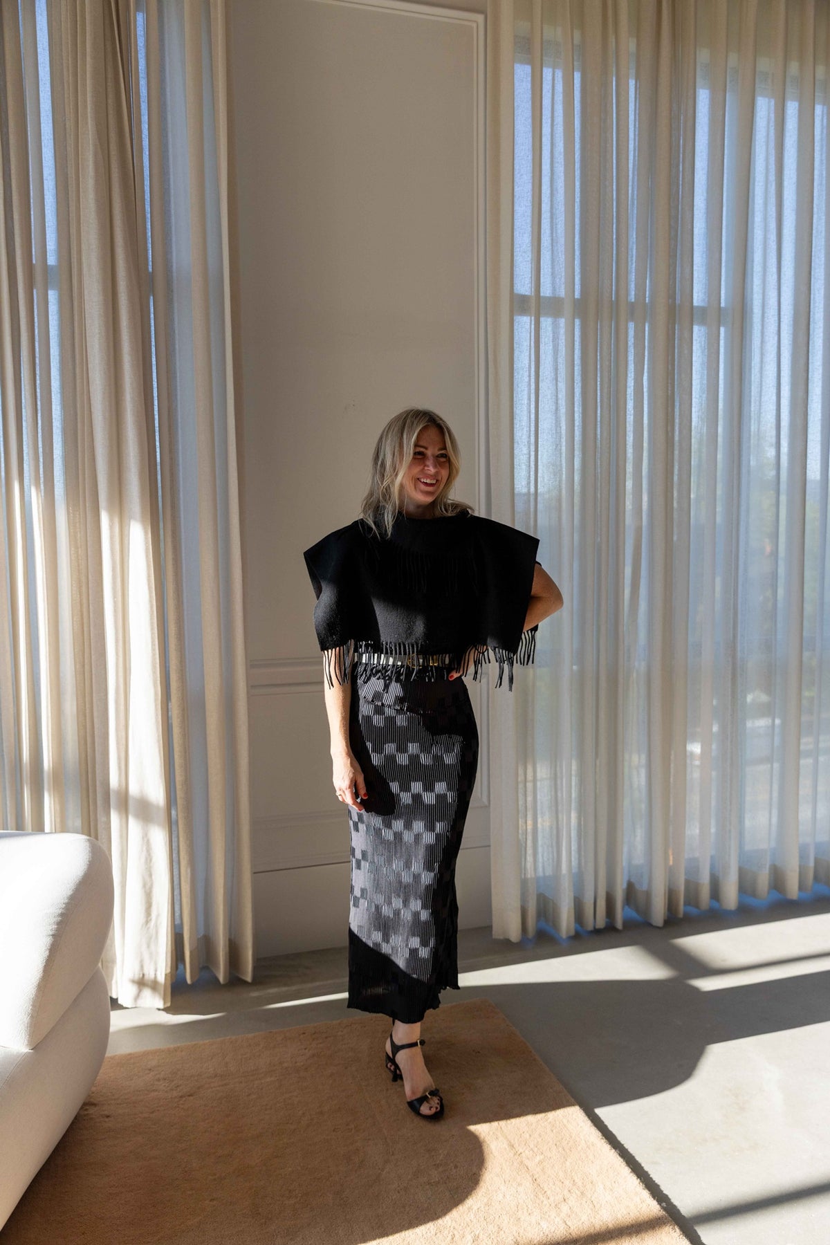 by Malene Birger Turtla in black, fringed wool cape scarf styled with a black pleated maxi skirt, full-length view