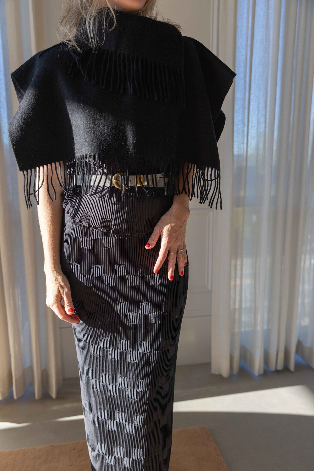 by Malene Birger Turtla in black wool, cape-shaped scarf with fringed trim worn over a black pleated skirt