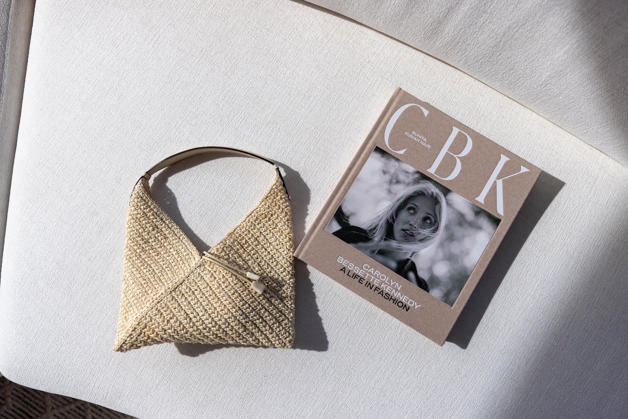 Hunting season bag next to CBK: Carolyn Bessette Kennedy Coffee table book on a white sofa.