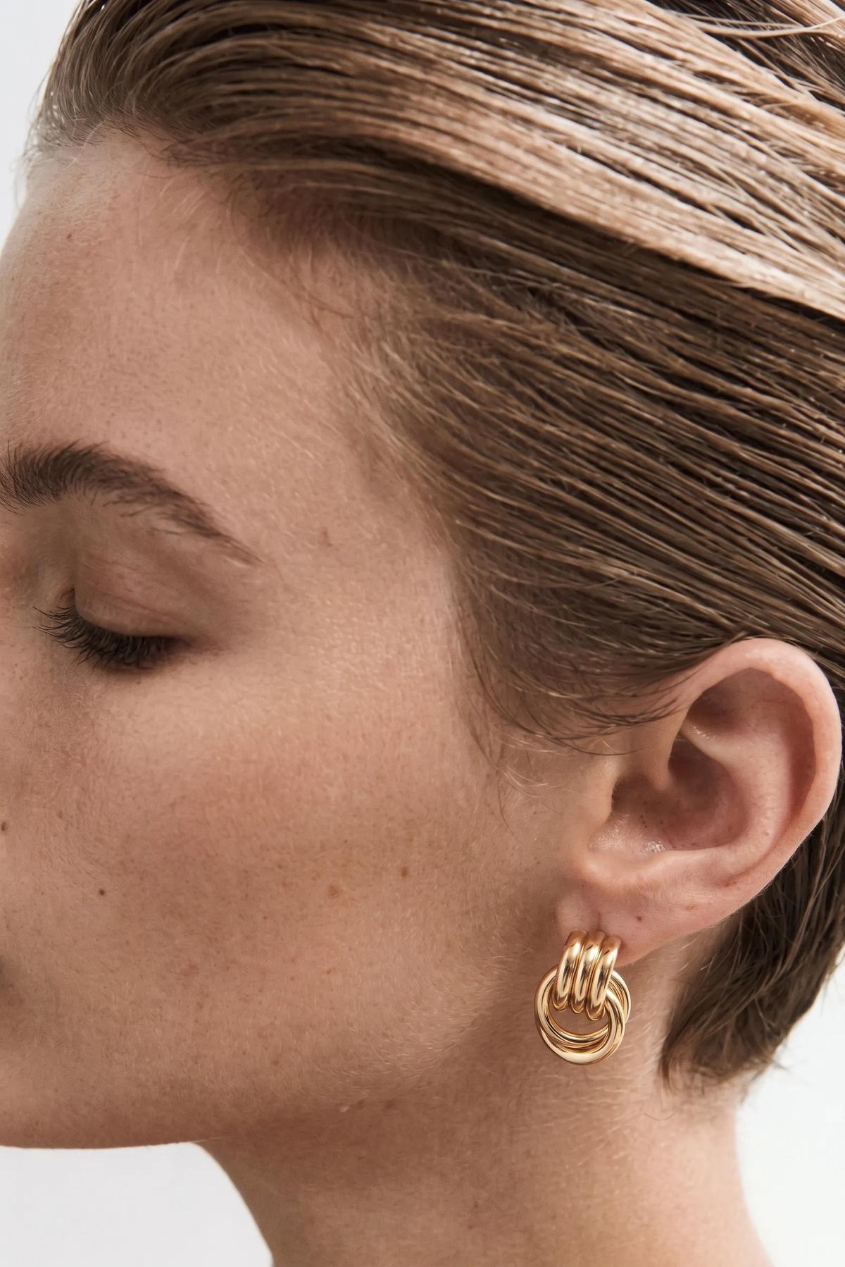 Close-up of a person wearing gold hoop earrings on a white background