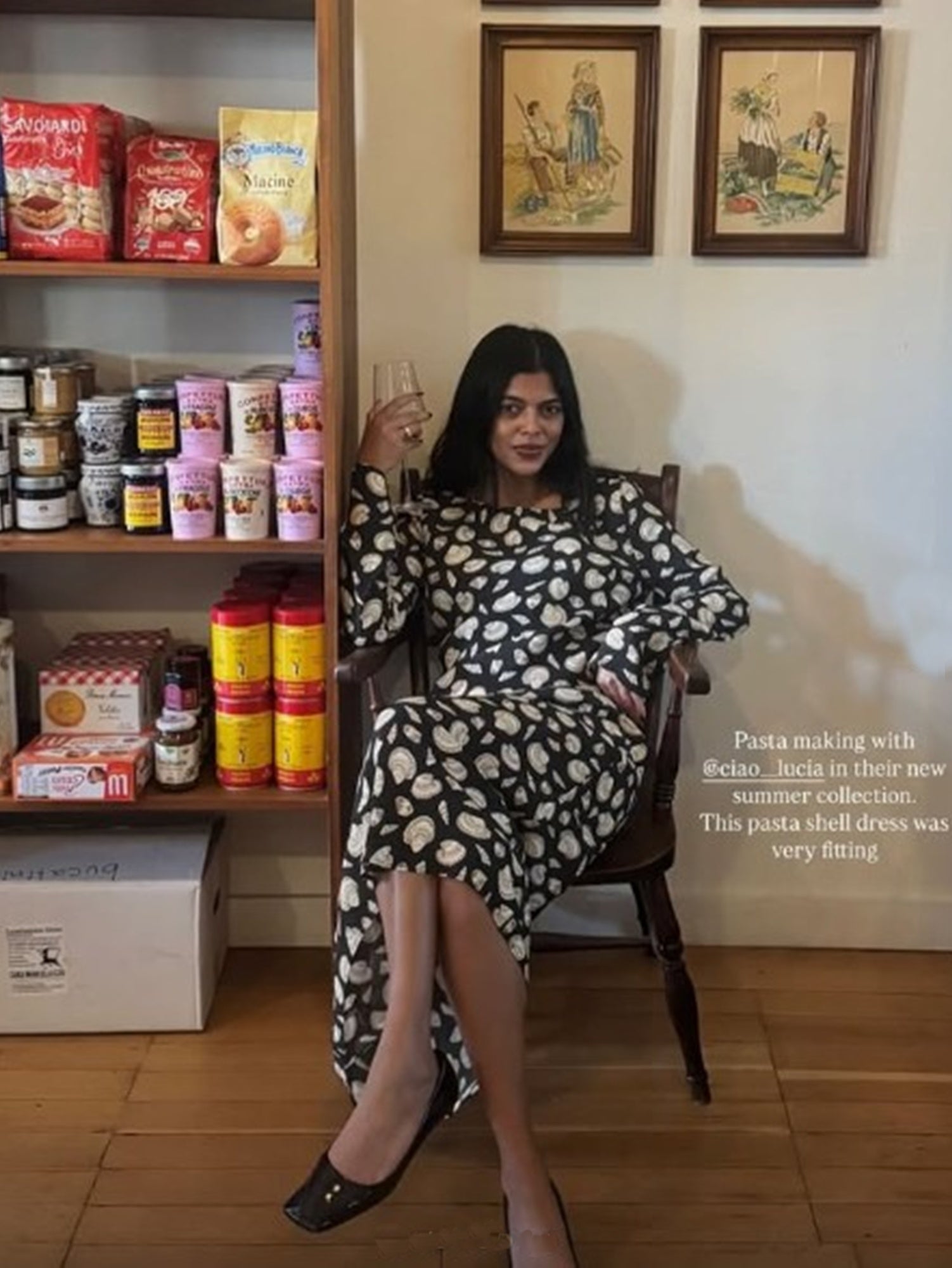 Woman in a patterned dress sitting on a chair next to a shelf with various products.