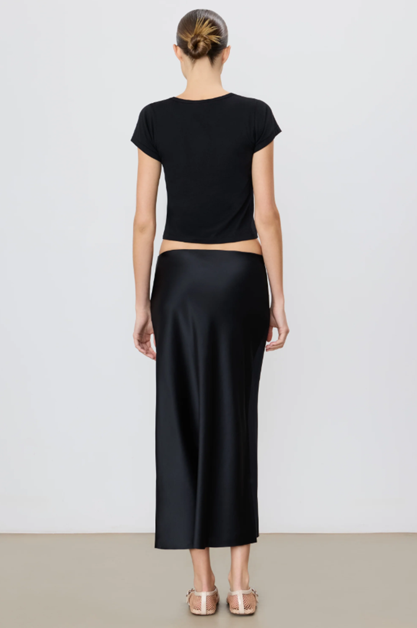 back of a model wearing a black outfit with a midi skirt on a plain background