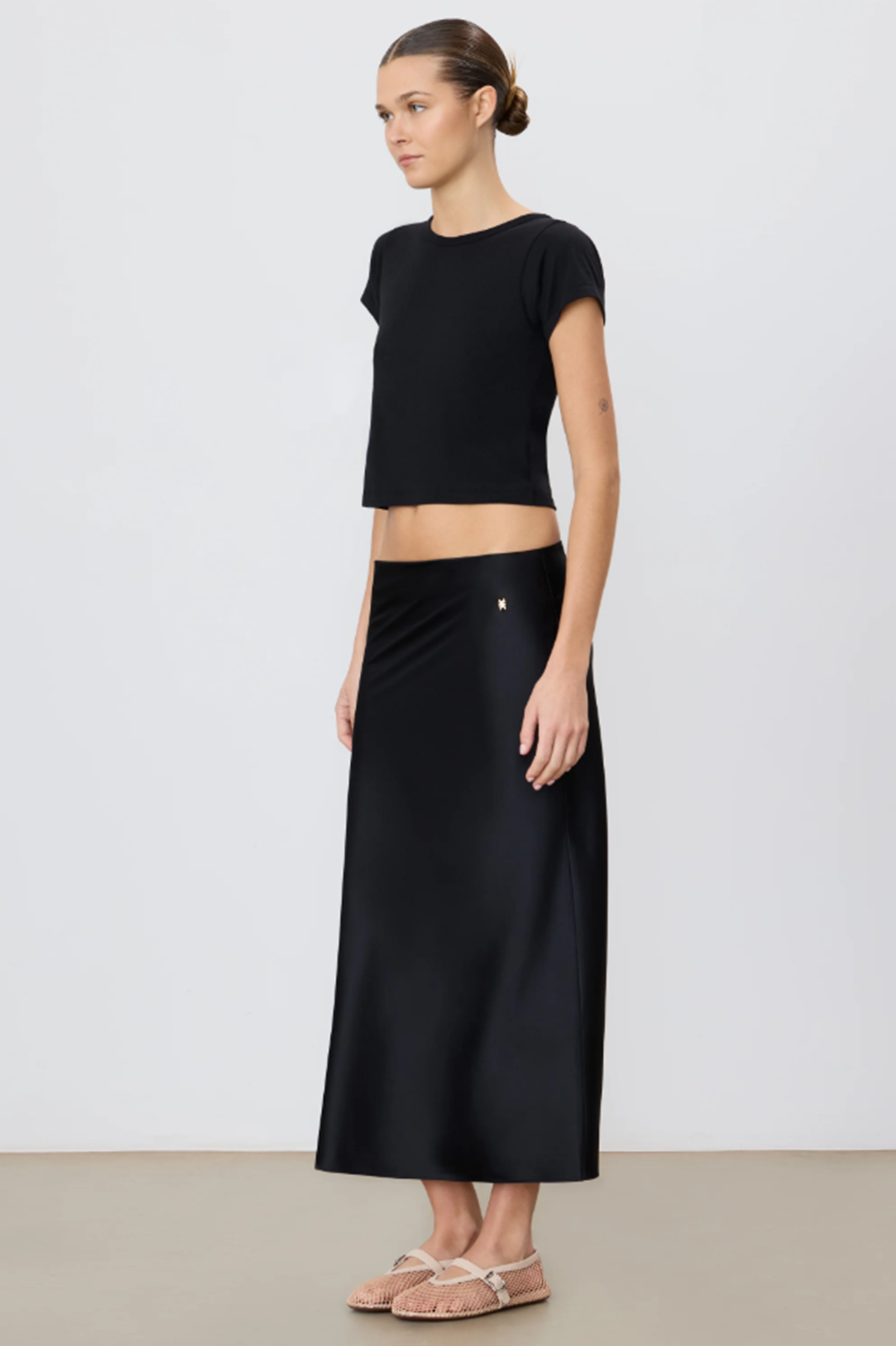 Woman wearing a black crop top and midi black skirt on a white background