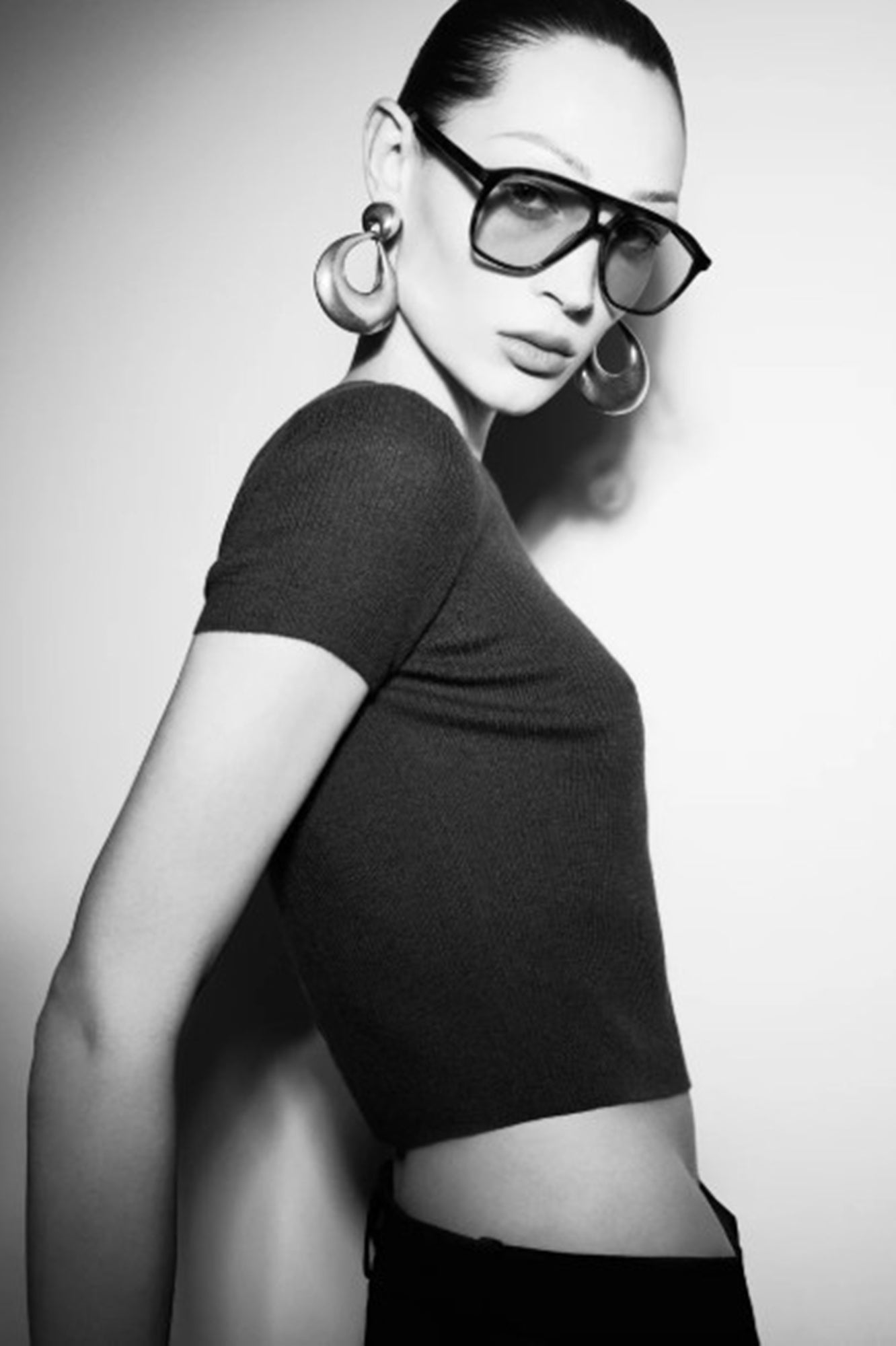 Black and white portrait of a woman wearing a black top and large hoop earrings.