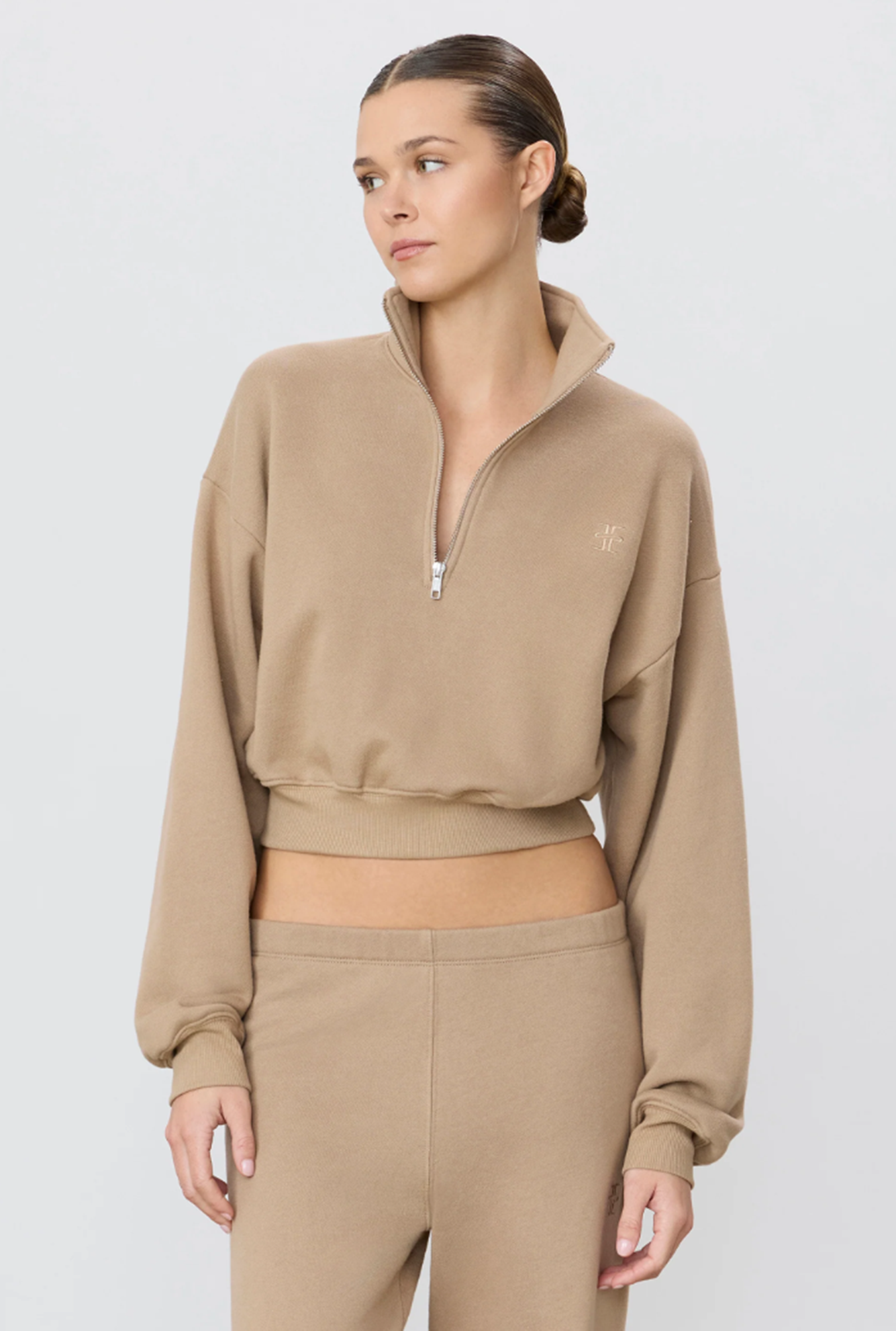 Woman wearing a beige cropped sweatshirt with a zipper on a light gray background