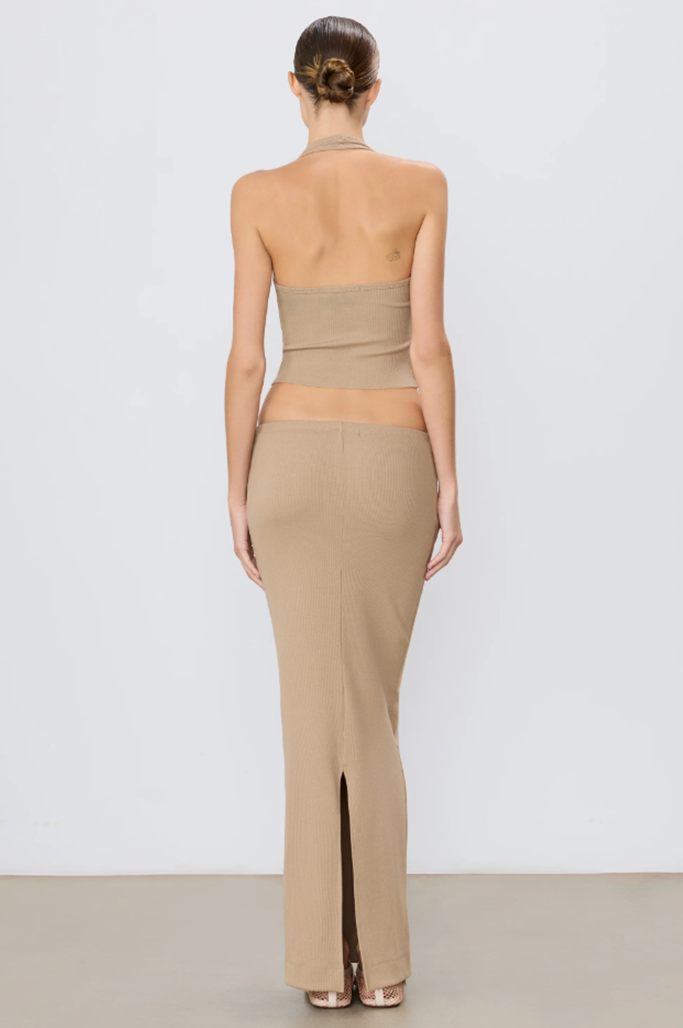 Woman wearing a taupe strapless top and taupe skirt on a light grey background