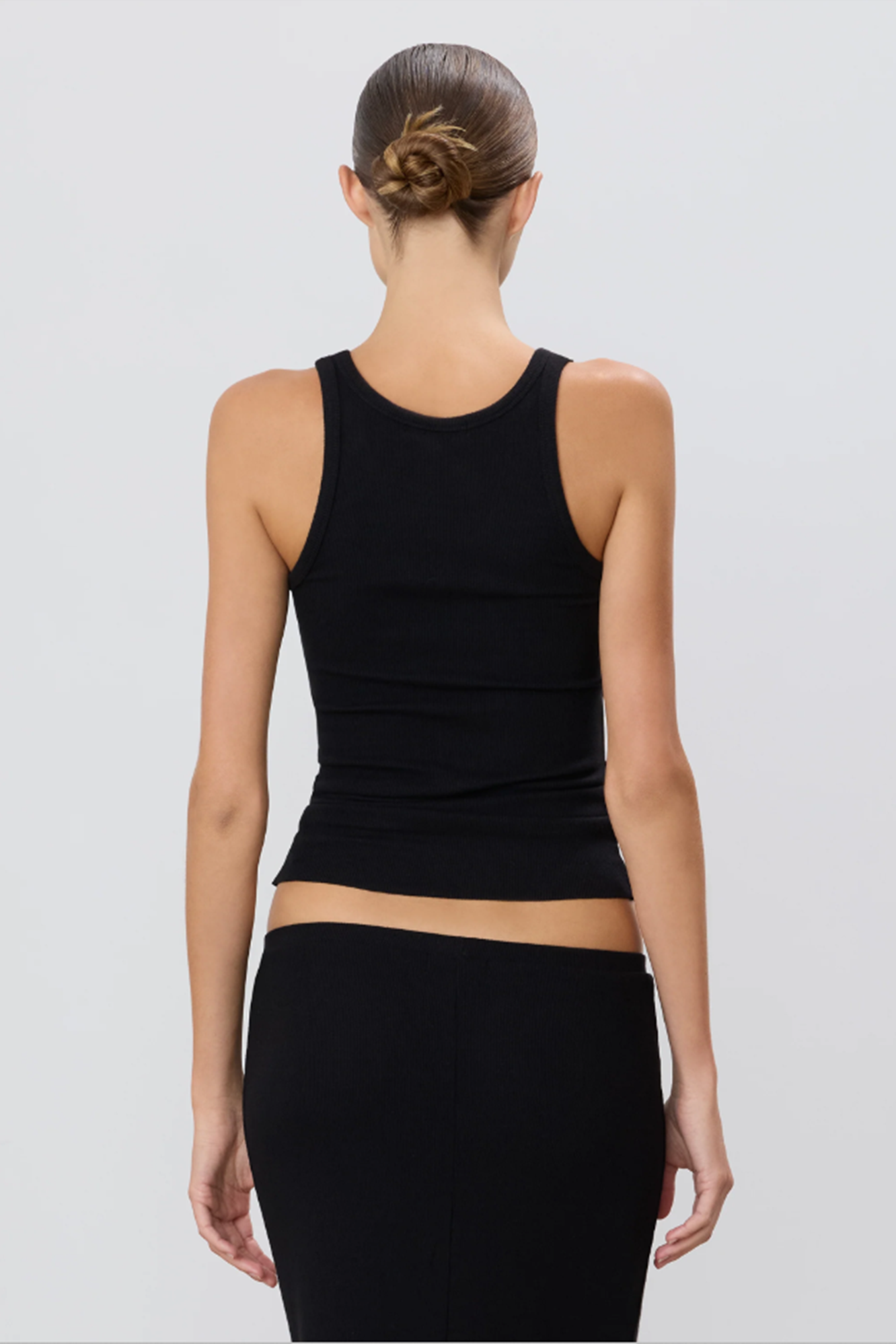 back of a model wearing a black sleeveless top and black skirt on a light gray background