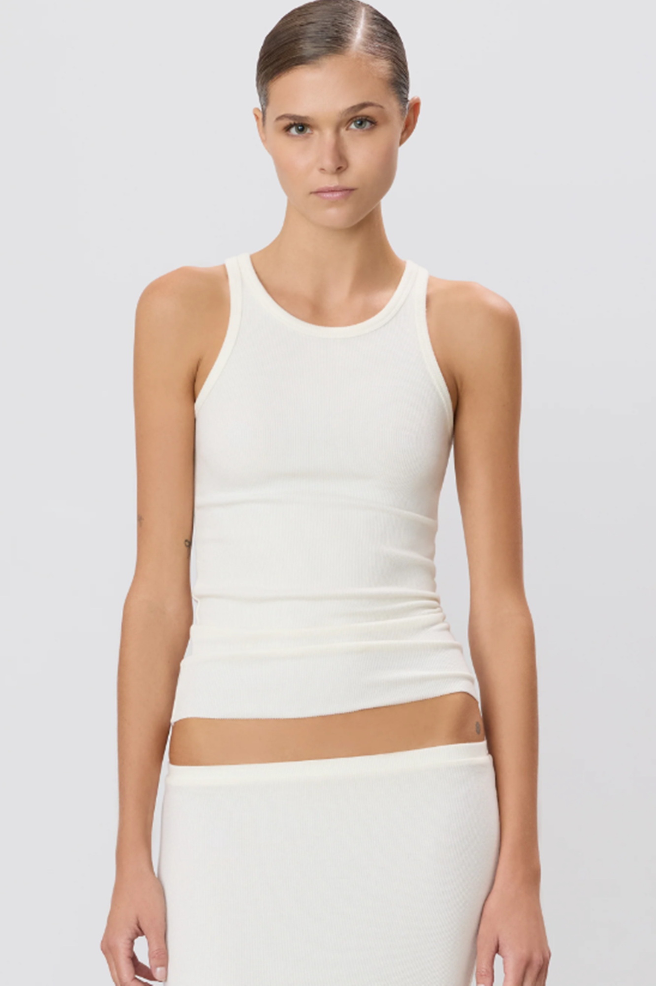Woman wearing a cream sleeveless tank top and skirt set on a light gray background