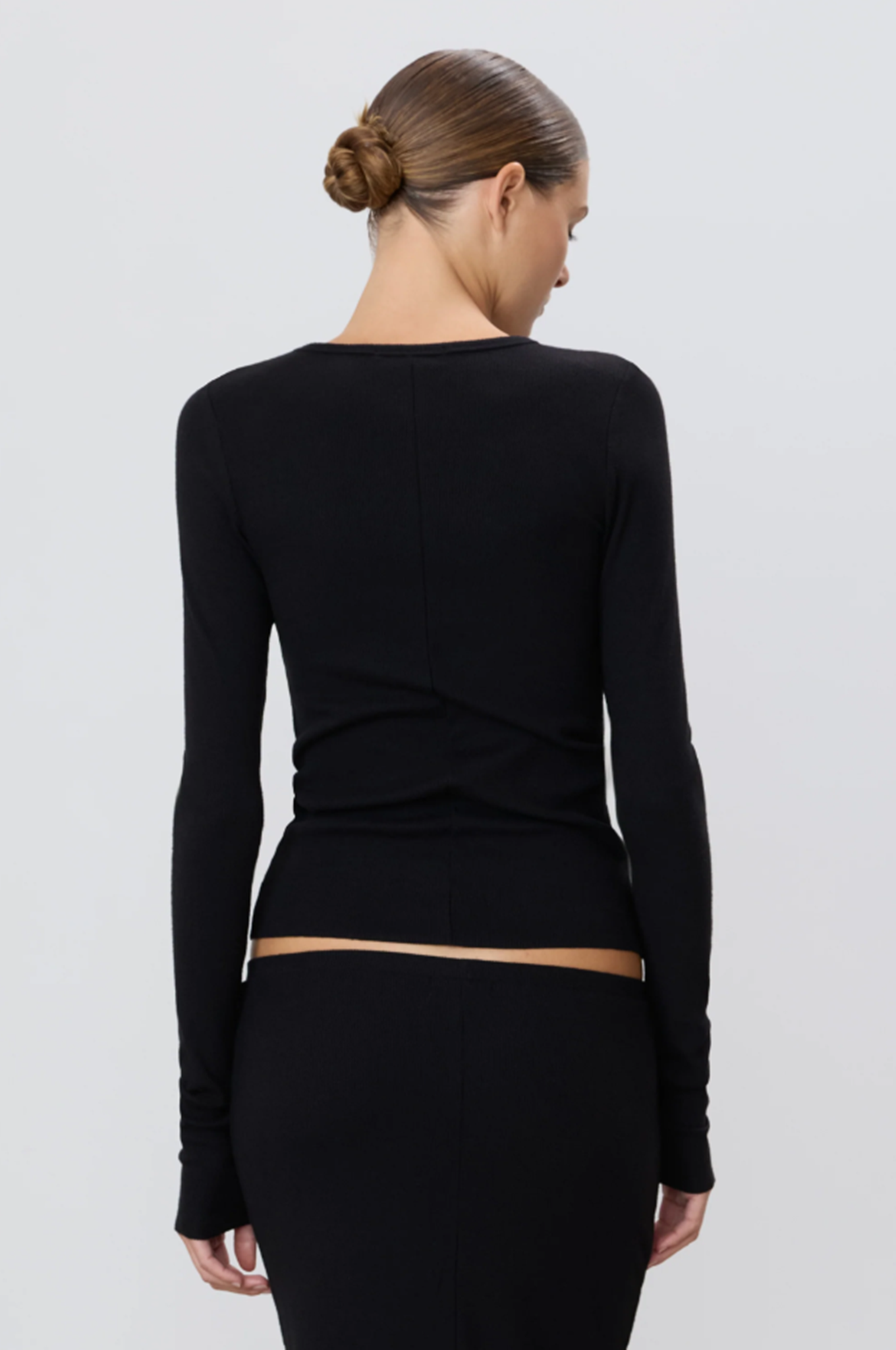 back of woman wearing a black long-sleeve top and skirt set on a light gray background