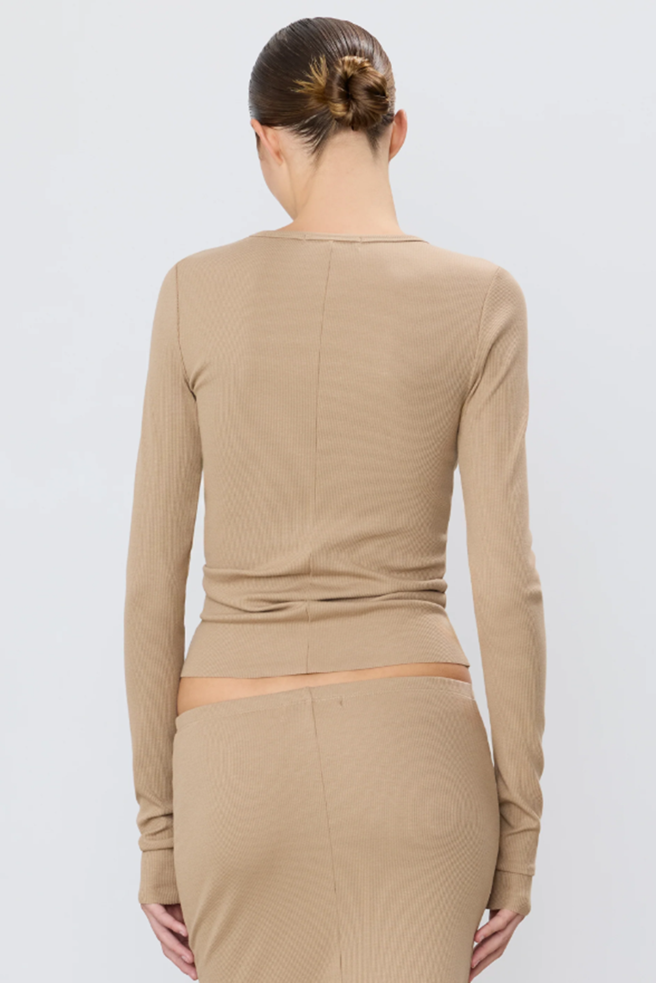 Back of woman wearing a beige long-sleeve top and skirt set on a light gray background
