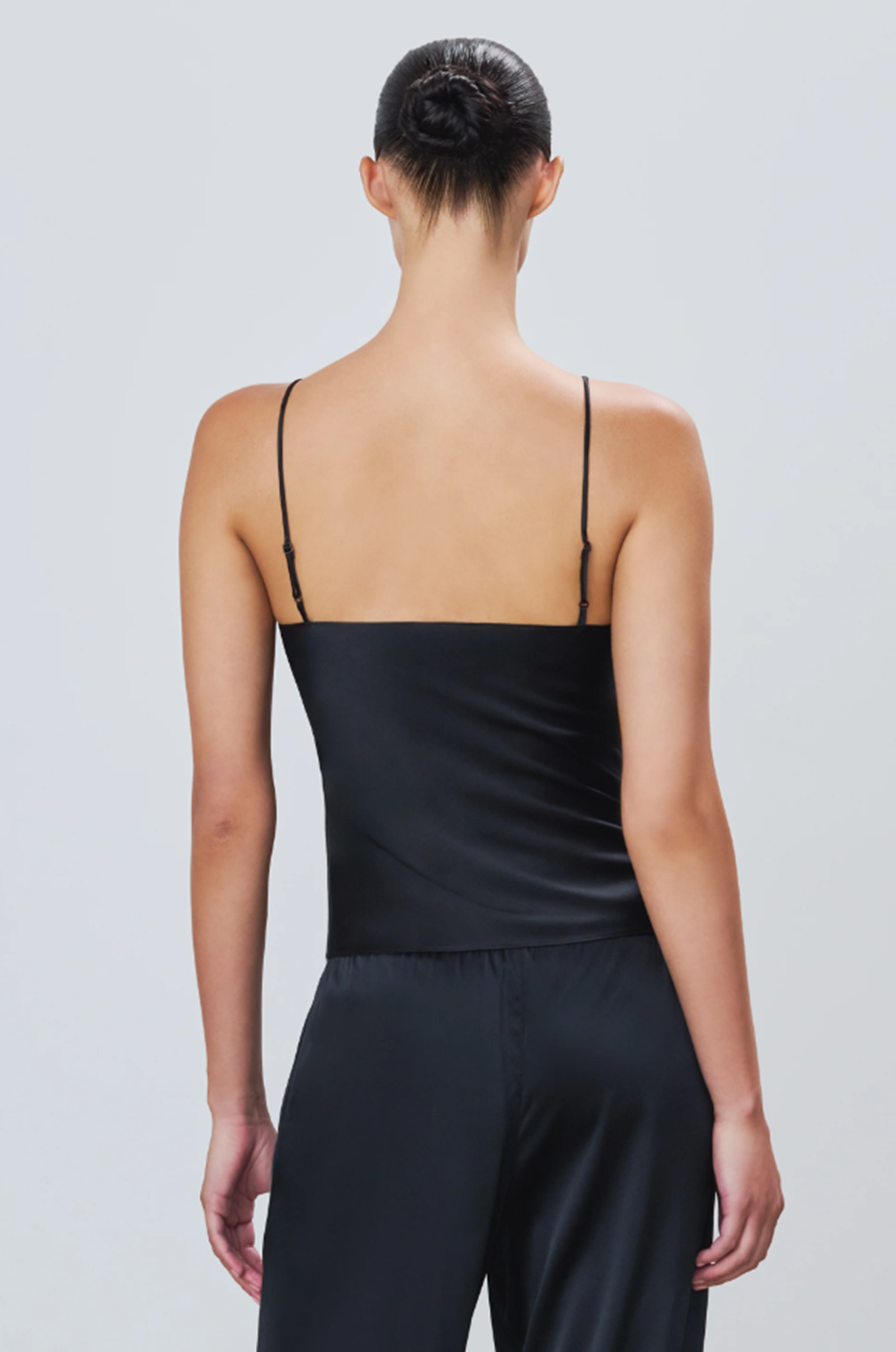 back of a model wearing a black silk camisole top and pants on a light gray background