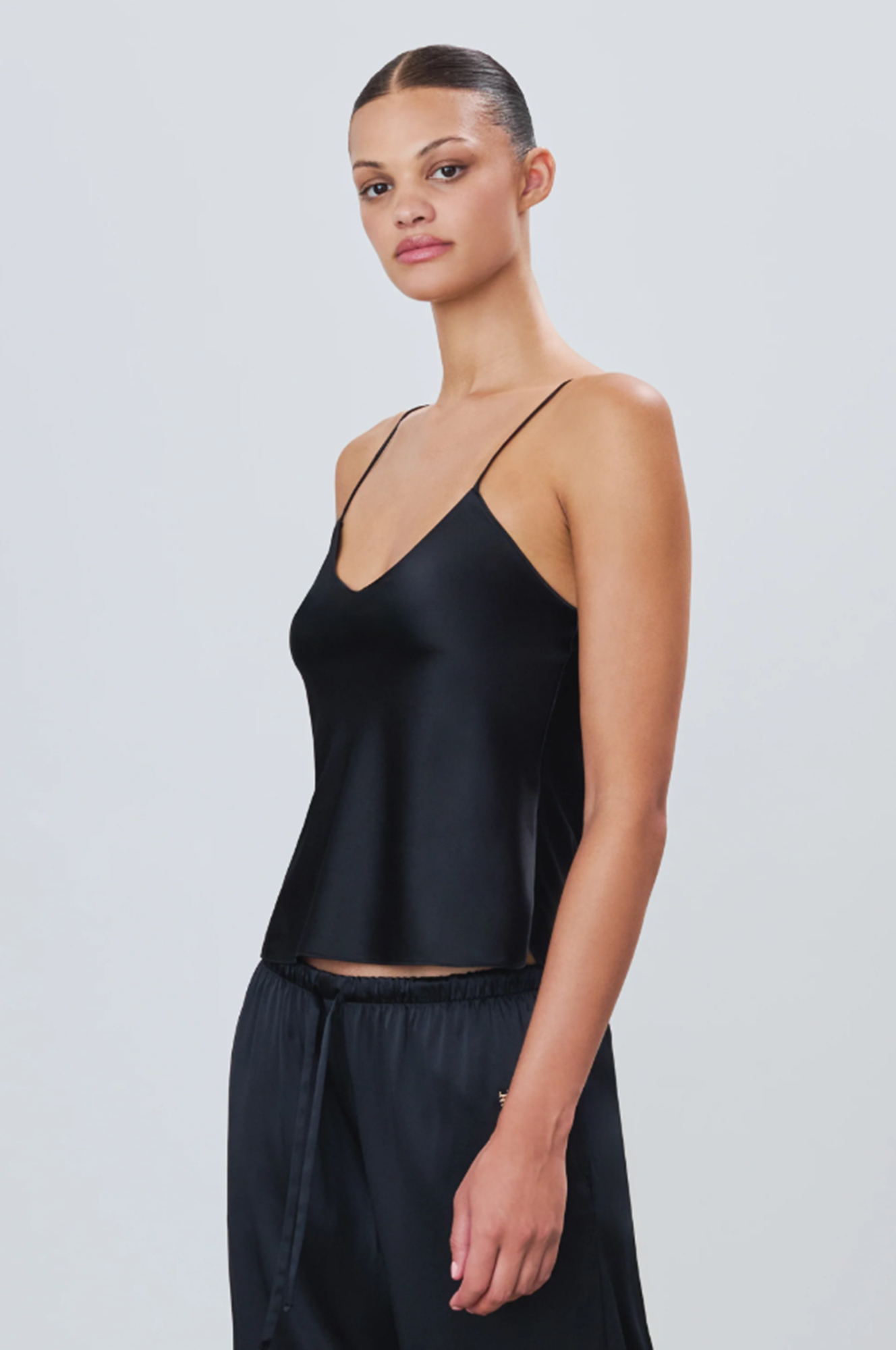 Woman wearing a black silk camisole and silk pants against a plain background