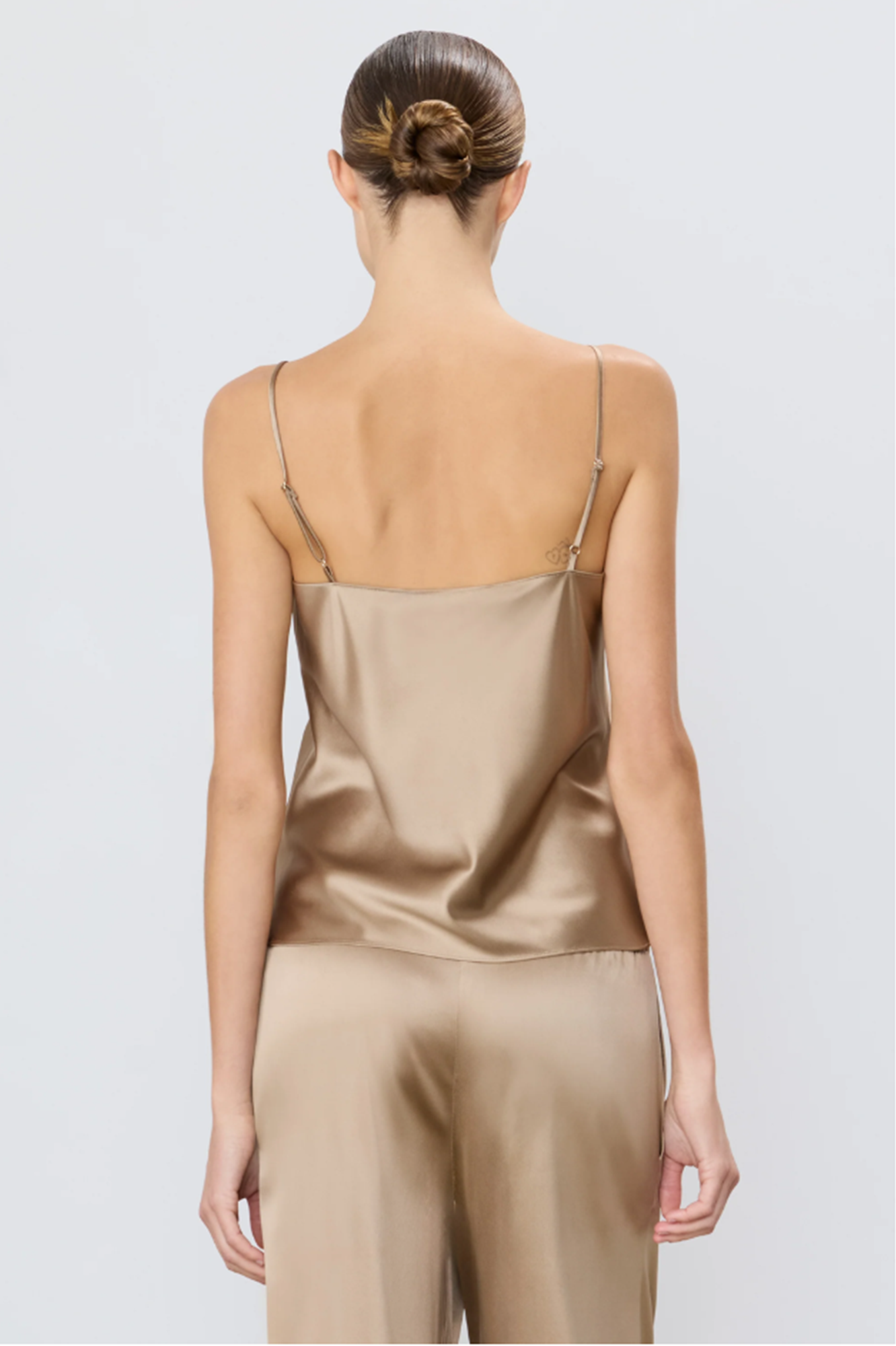 back of a woman wearing a taupe silk camisole and taupe pants on a white background