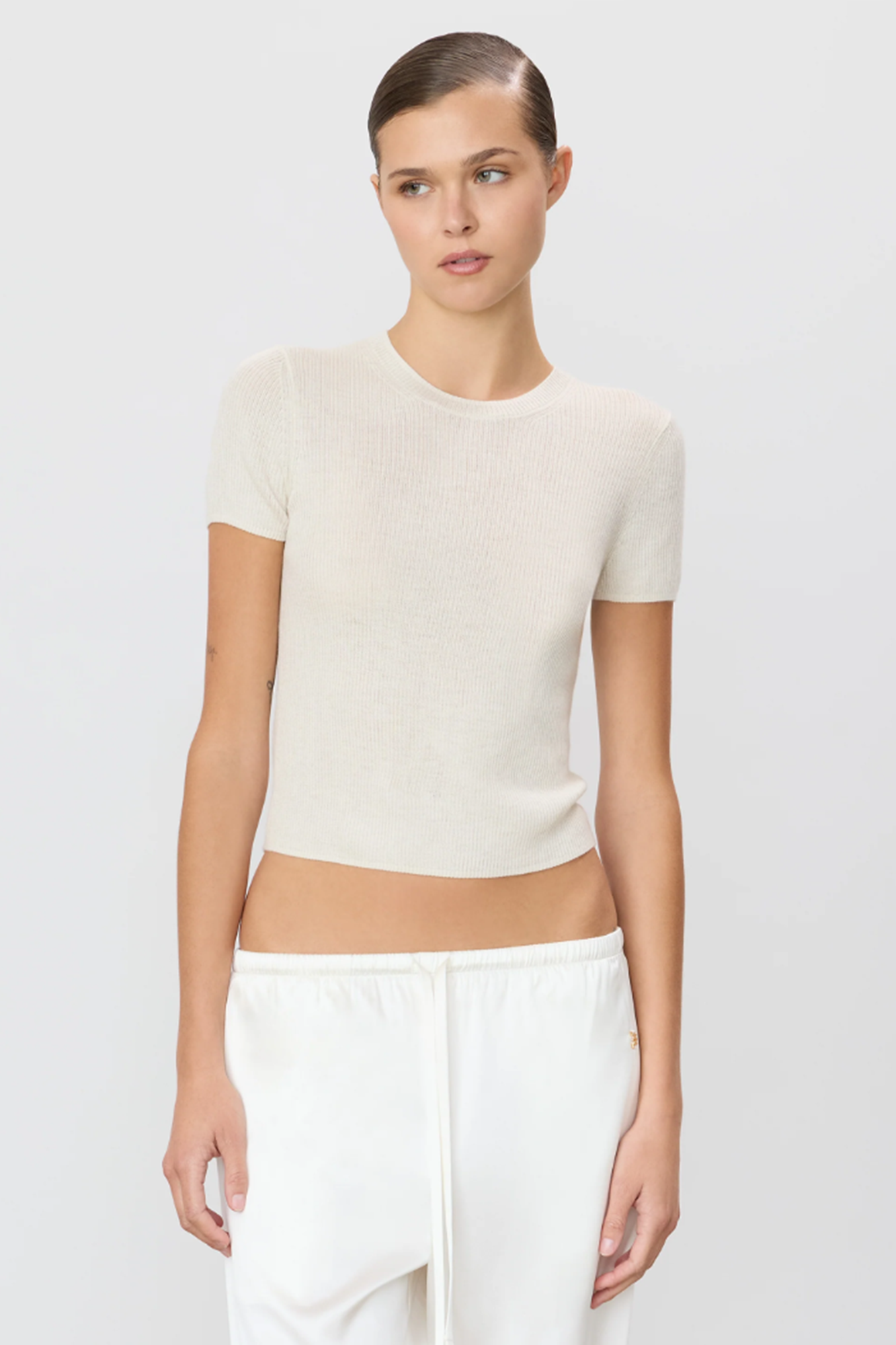 Woman wearing a bone cashmere cropped sweater and pants on a plain background