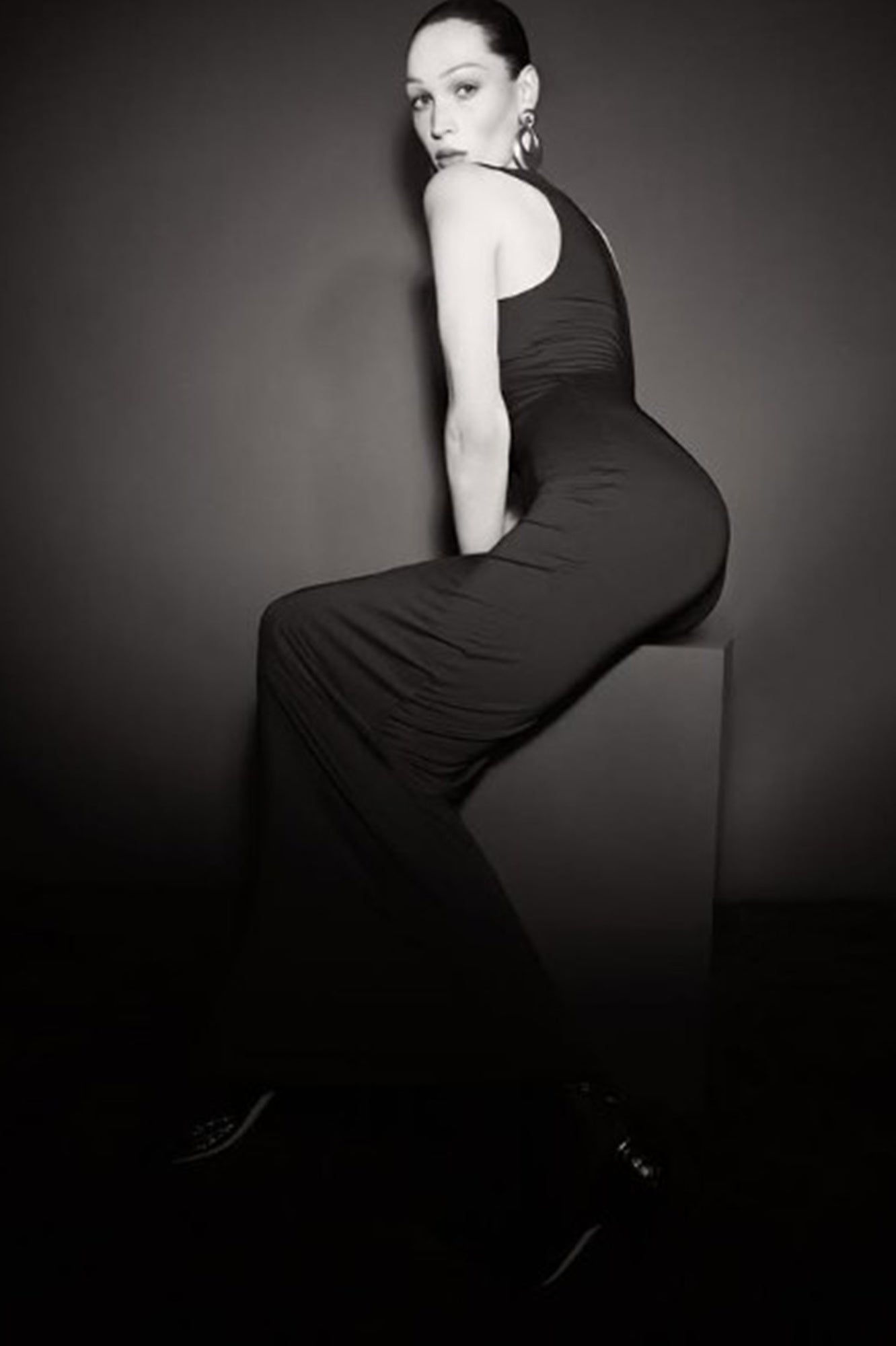 Person wearing a black dress sitting on a block against a dark background