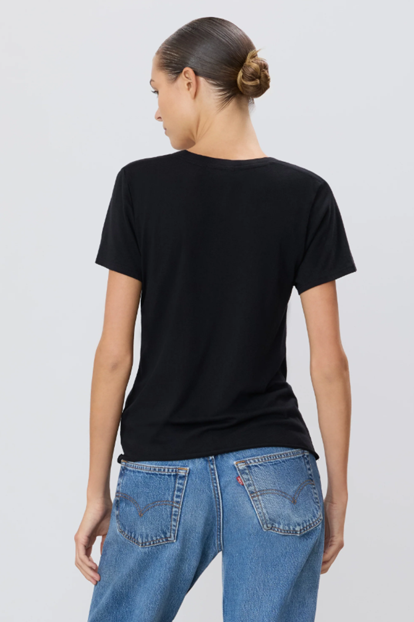 back of model wearing a black t-shirt and blue jeans on a light gray background