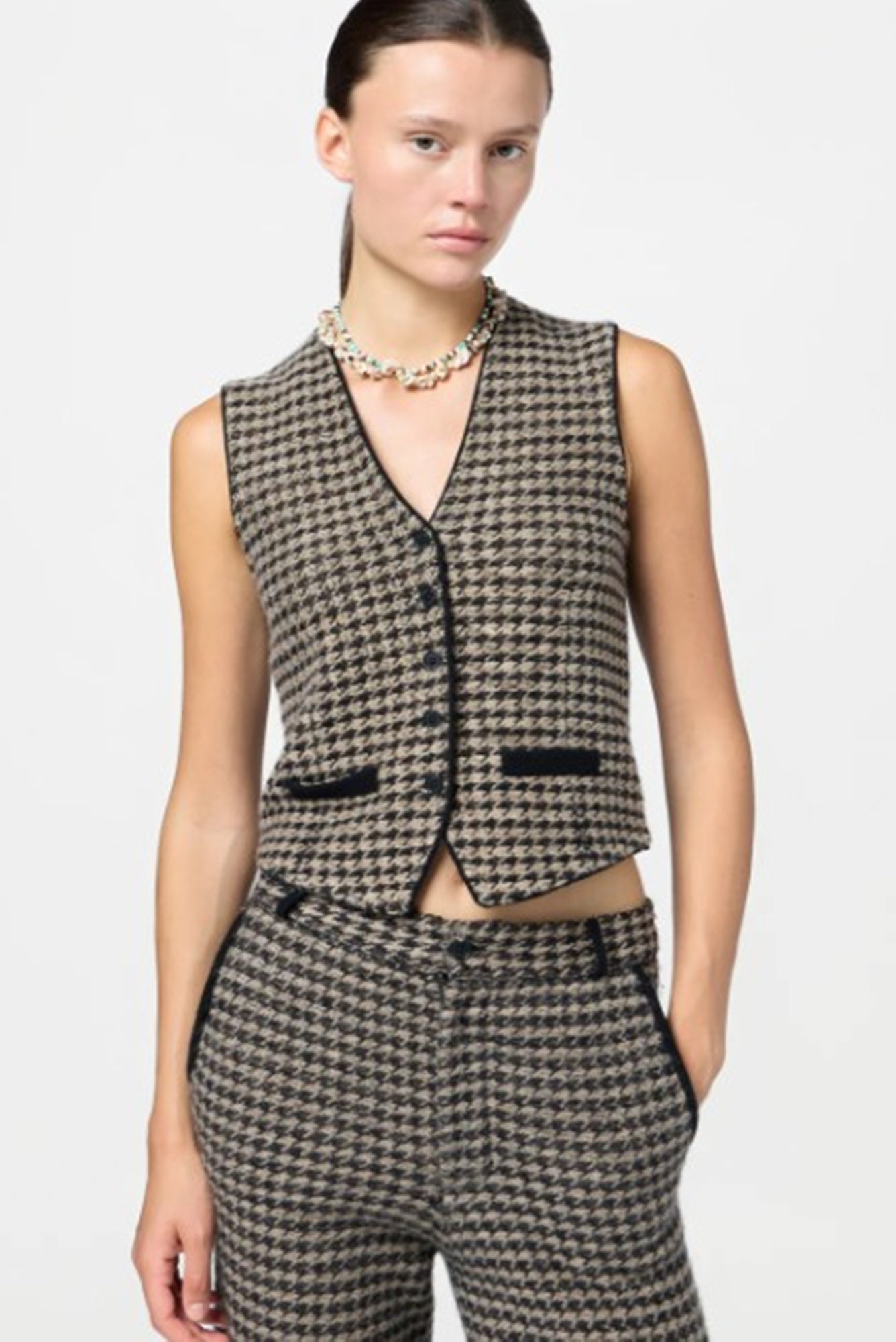 Woman wearing a houndstooth patterned vest and pants on a white background