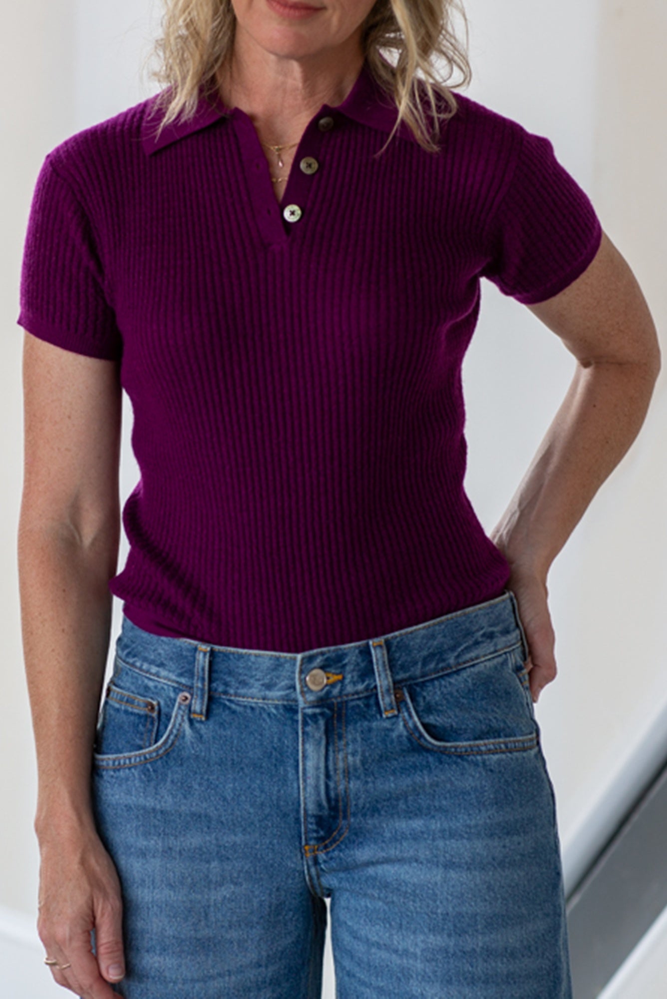Woman wearing a purple ribbed polo shirt and blue jeans against a white background