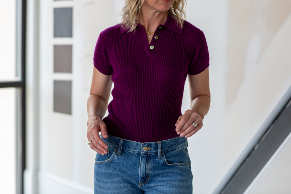 Woman wearing a purple ribbed shirt and blue jeans indoors.