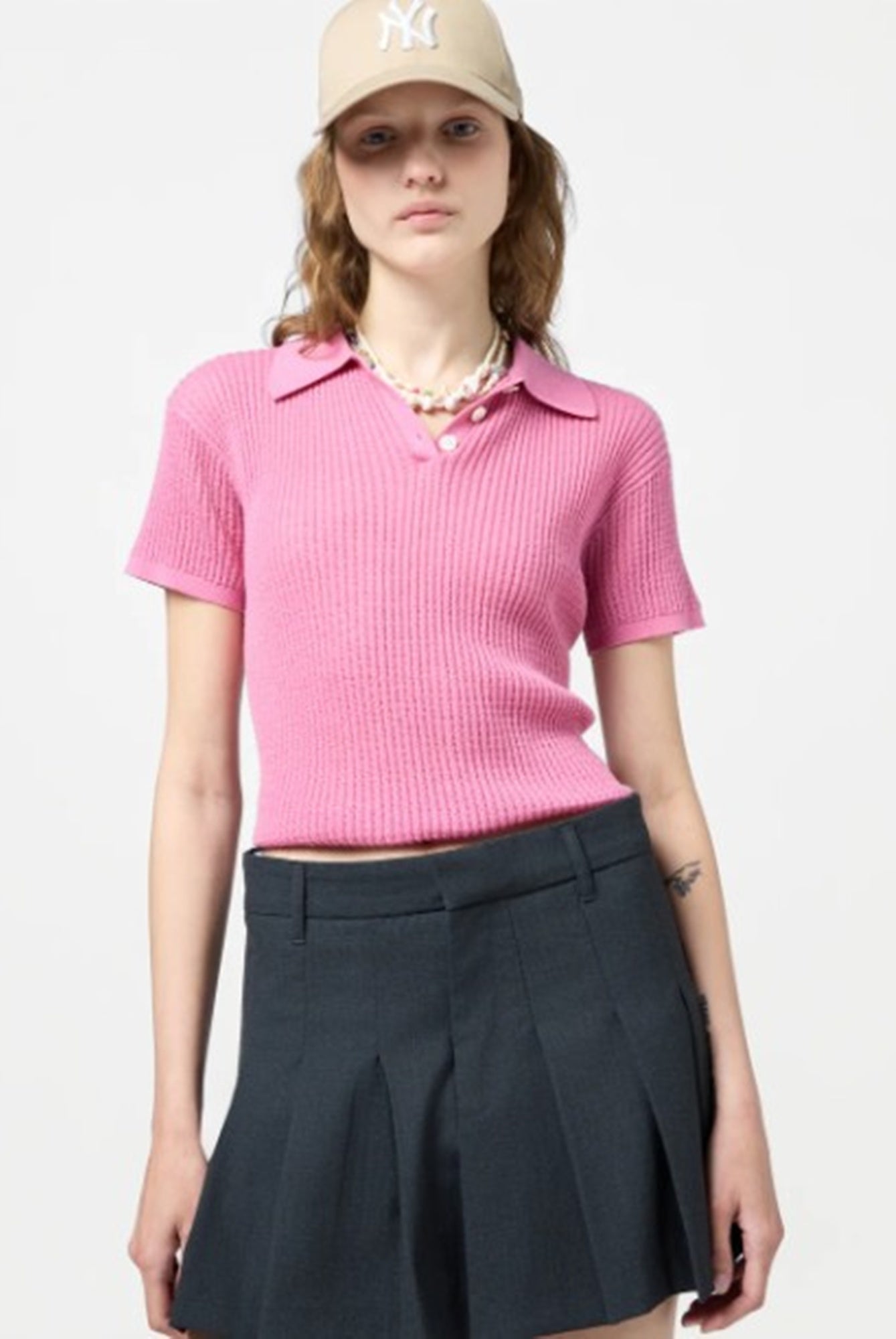 Person wearing a pink polo shirt and black skirt with a beige cap on a white background