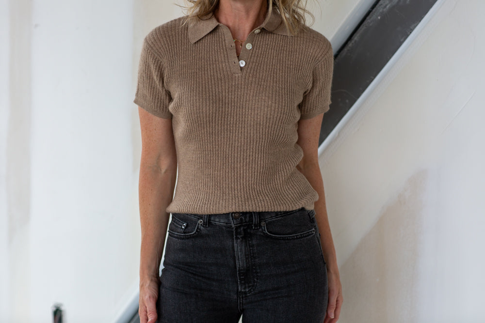 Person wearing a brown ribbed polo shirt and black jeans indoors.