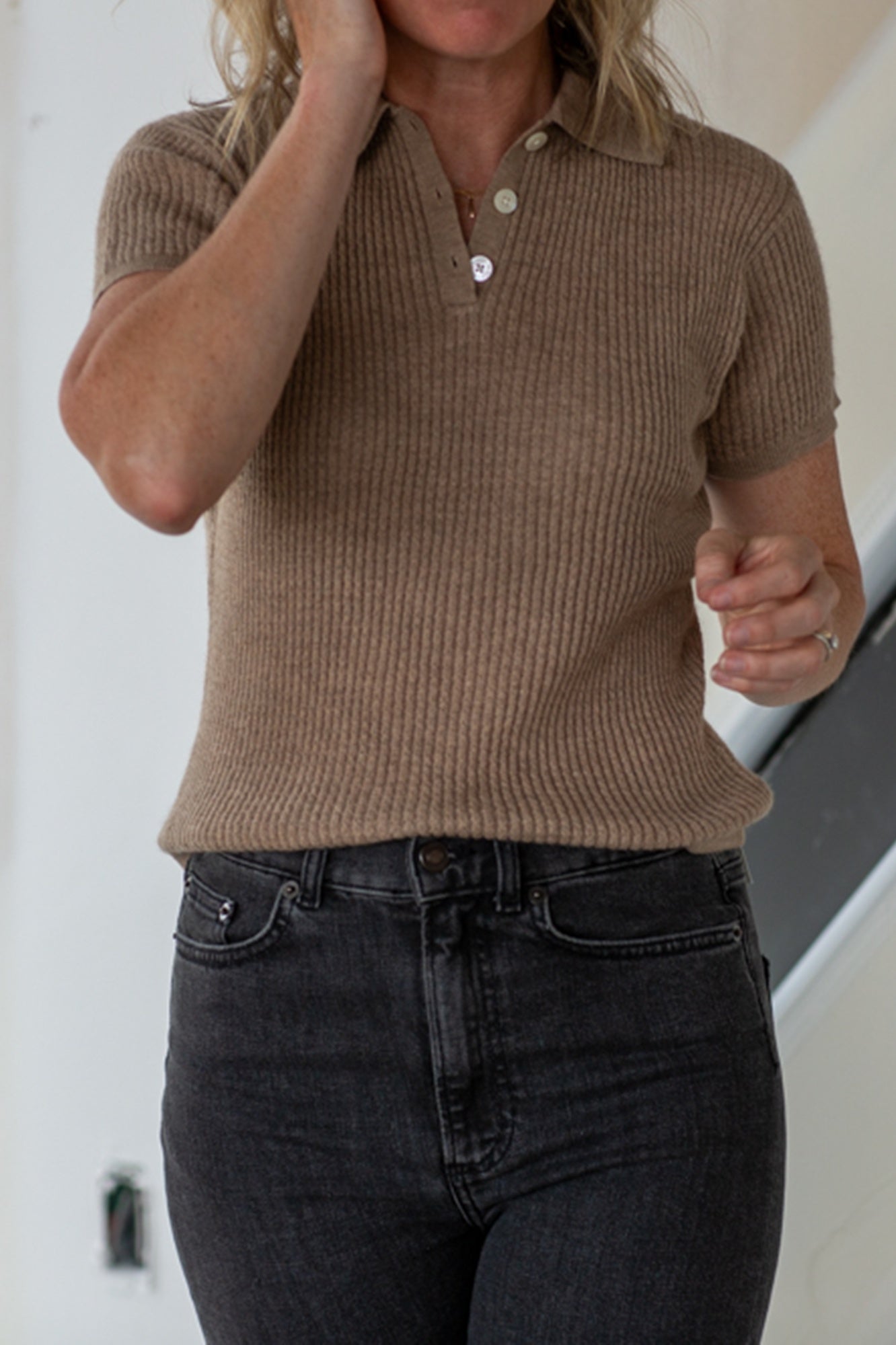 Person wearing a brown ribbed knit polo shirt and dark jeans against a neutral background