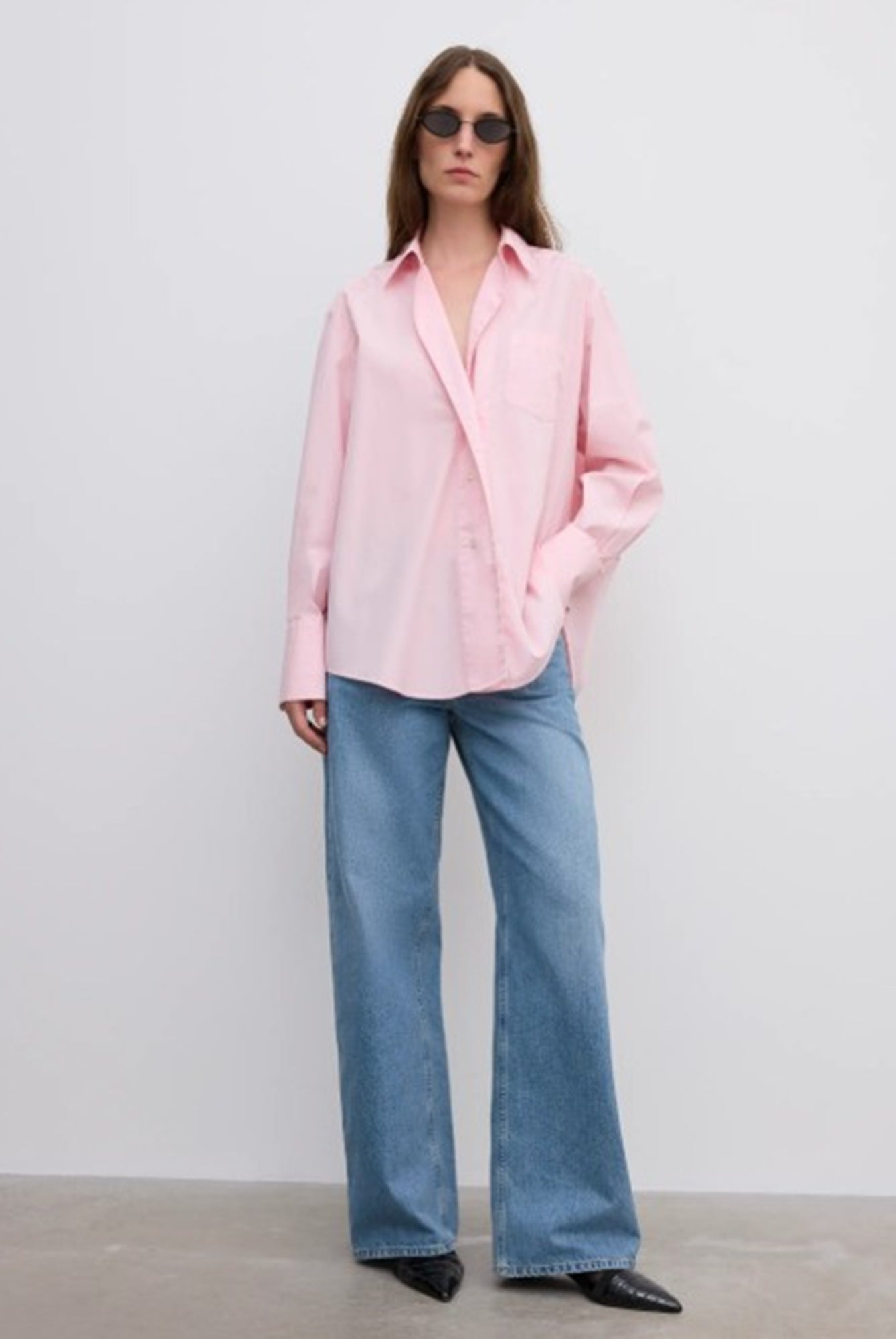 Person wearing a pink shirt and blue jeans against a white background