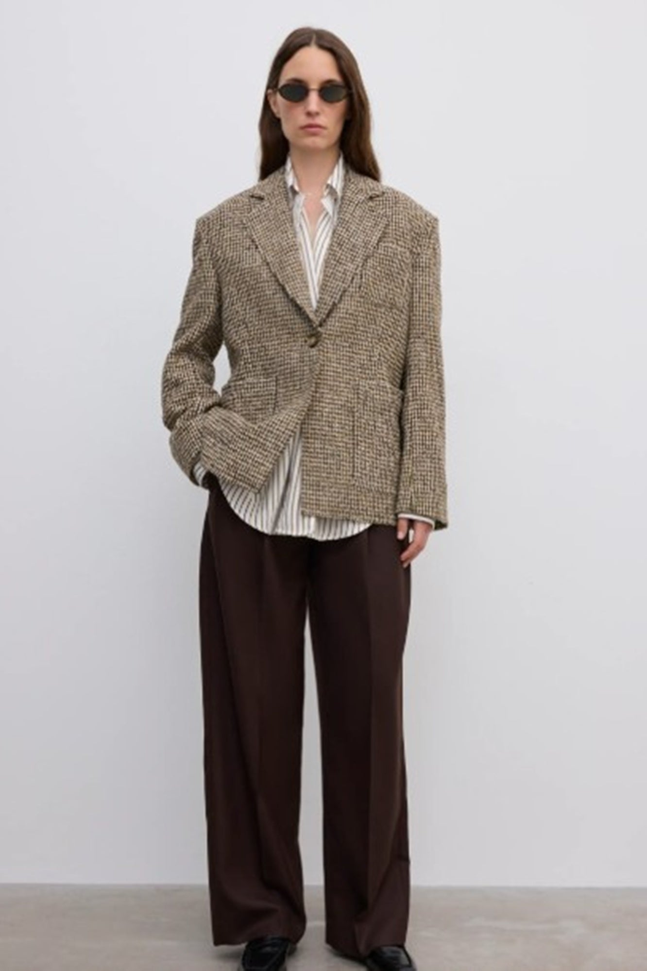 Person wearing a textured blazer and brown pants against a white background