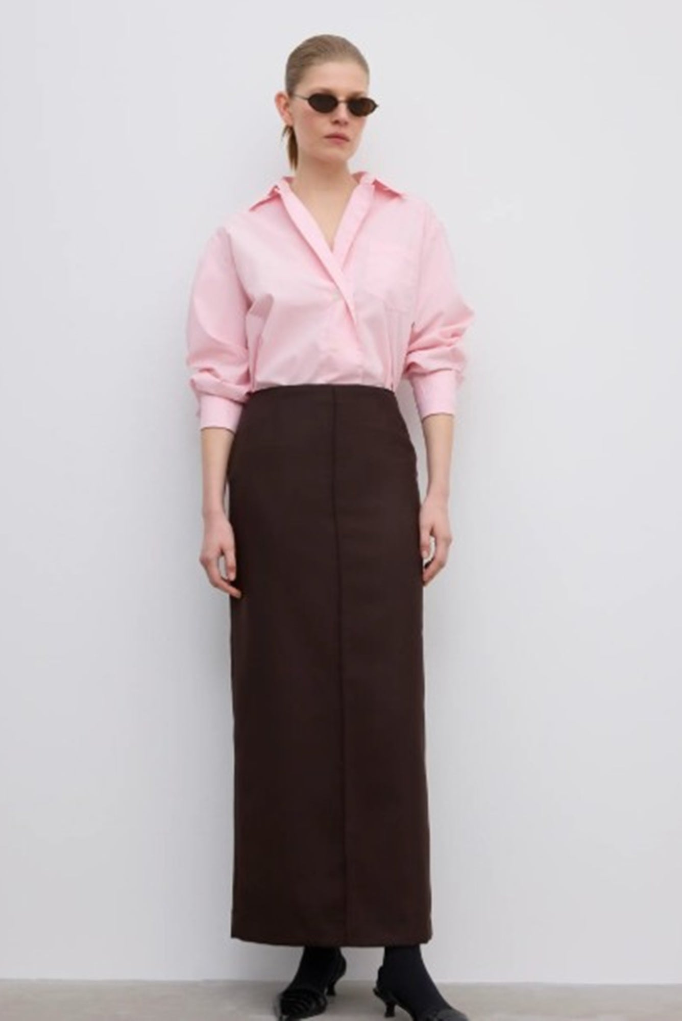 Woman wearing a pink blouse and brown skirt against a white background