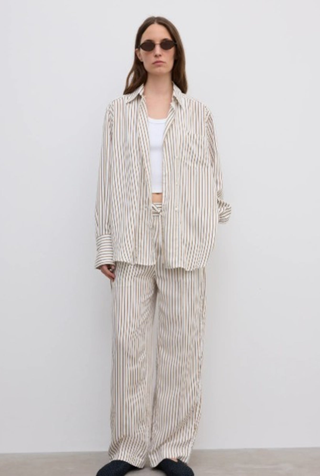 Woman wearing a striped suit and sunglasses against a white background