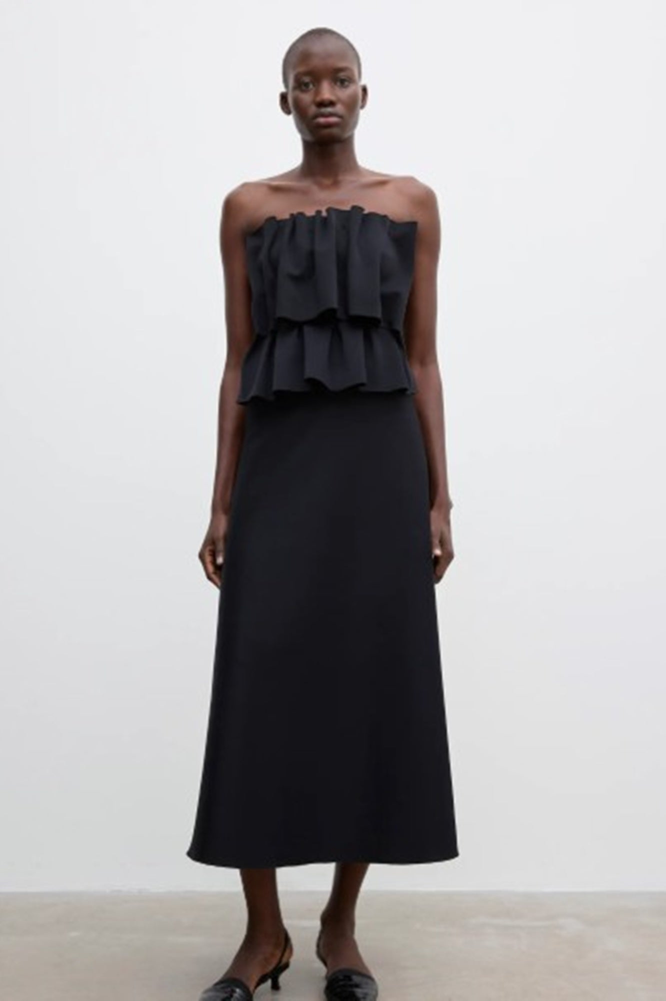 Woman wearing a black strapless dress with ruffled top on a white background