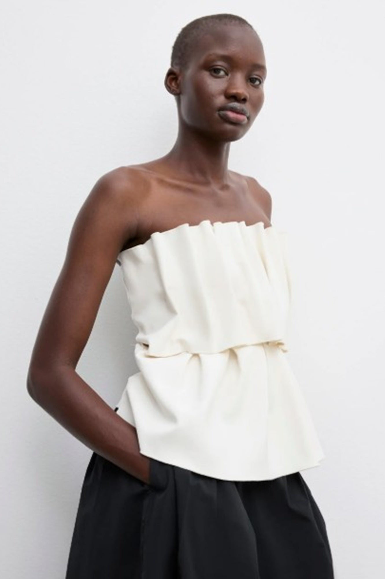 Woman wearing a strapless white top with ruffles against a plain background