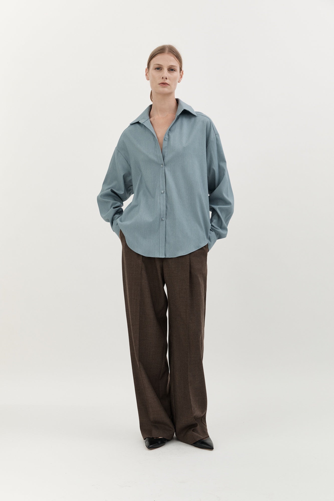 Person wearing a light blue shirt and brown pants on a white background
