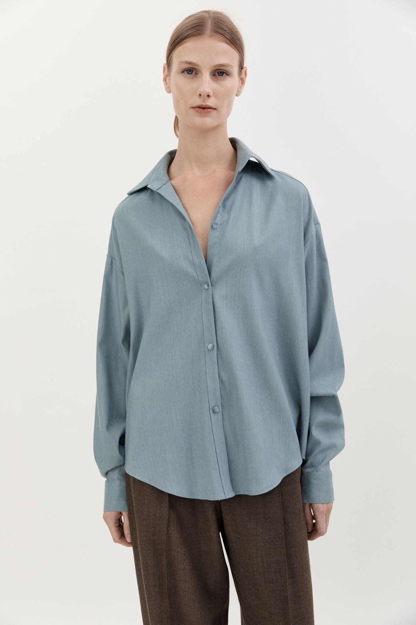 Woman wearing a light blue shirt and brown pants on a white background