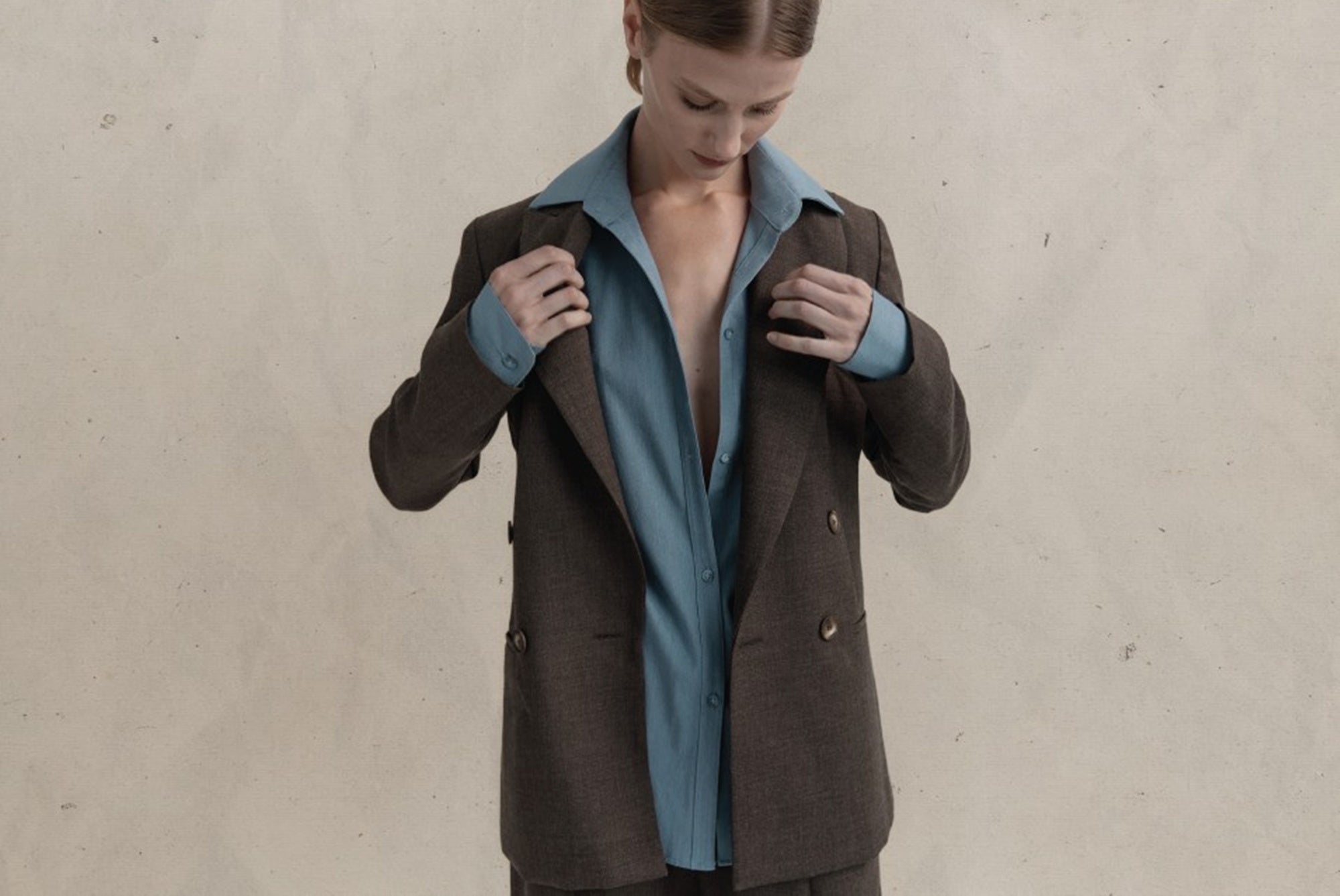 Person wearing a brown coat over a blue shirt against a beige background