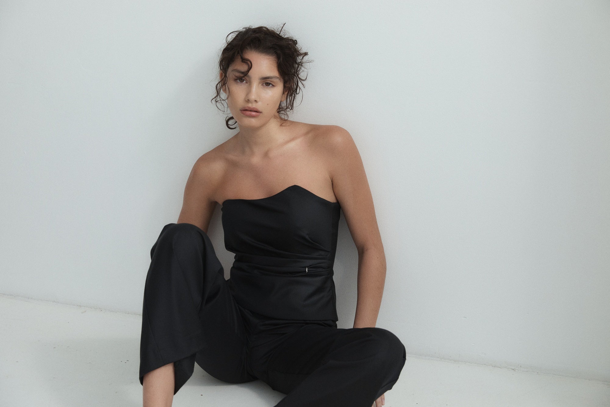 Woman wearing a black strapless outfit sitting on a white surface.