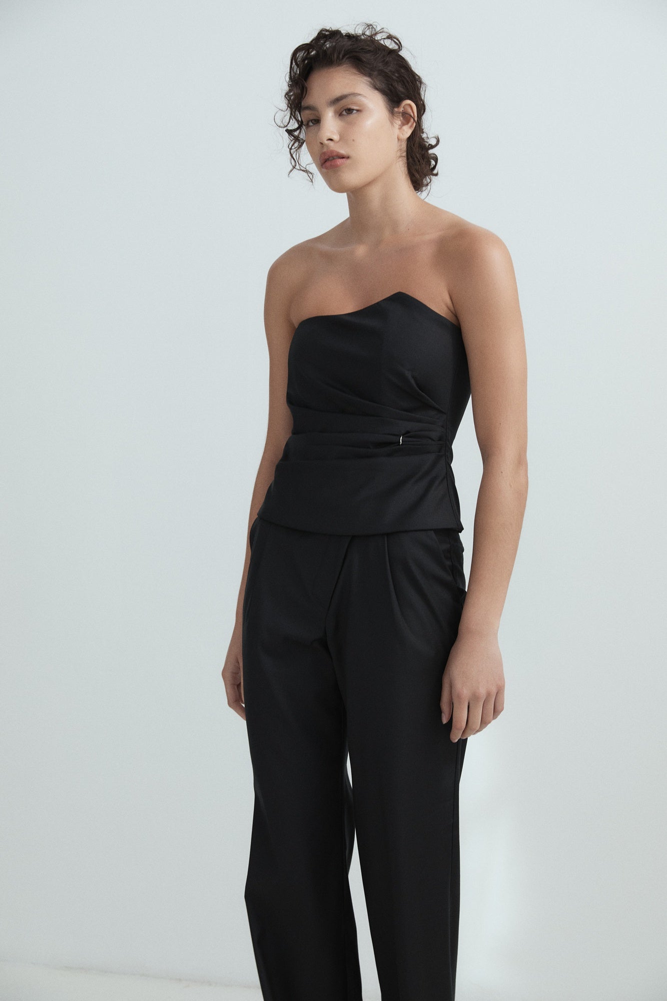 Woman wearing a black strapless jumpsuit on a white background