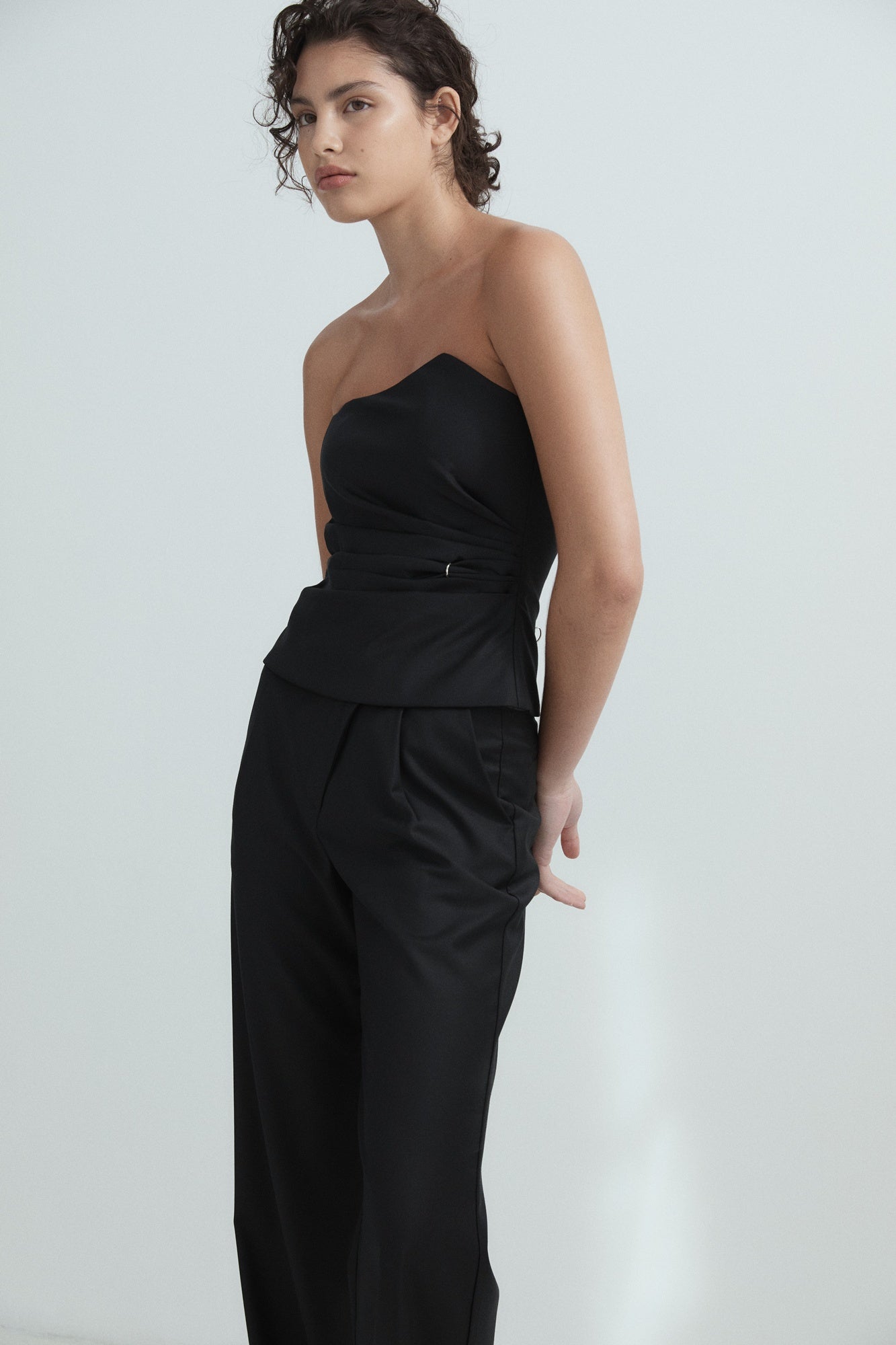 Woman wearing a black strapless top and high-waisted pants against a white background