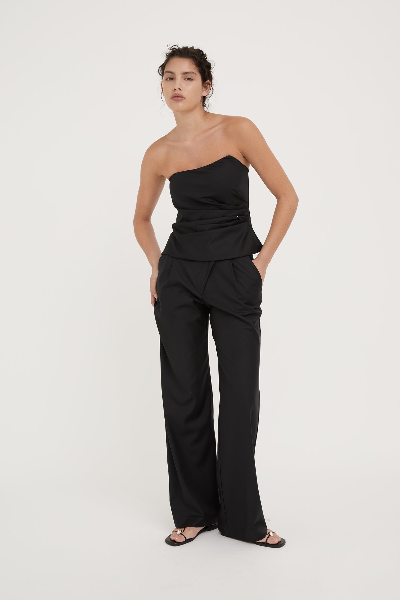 Woman wearing a black strapless top and wide-leg pants on a white background