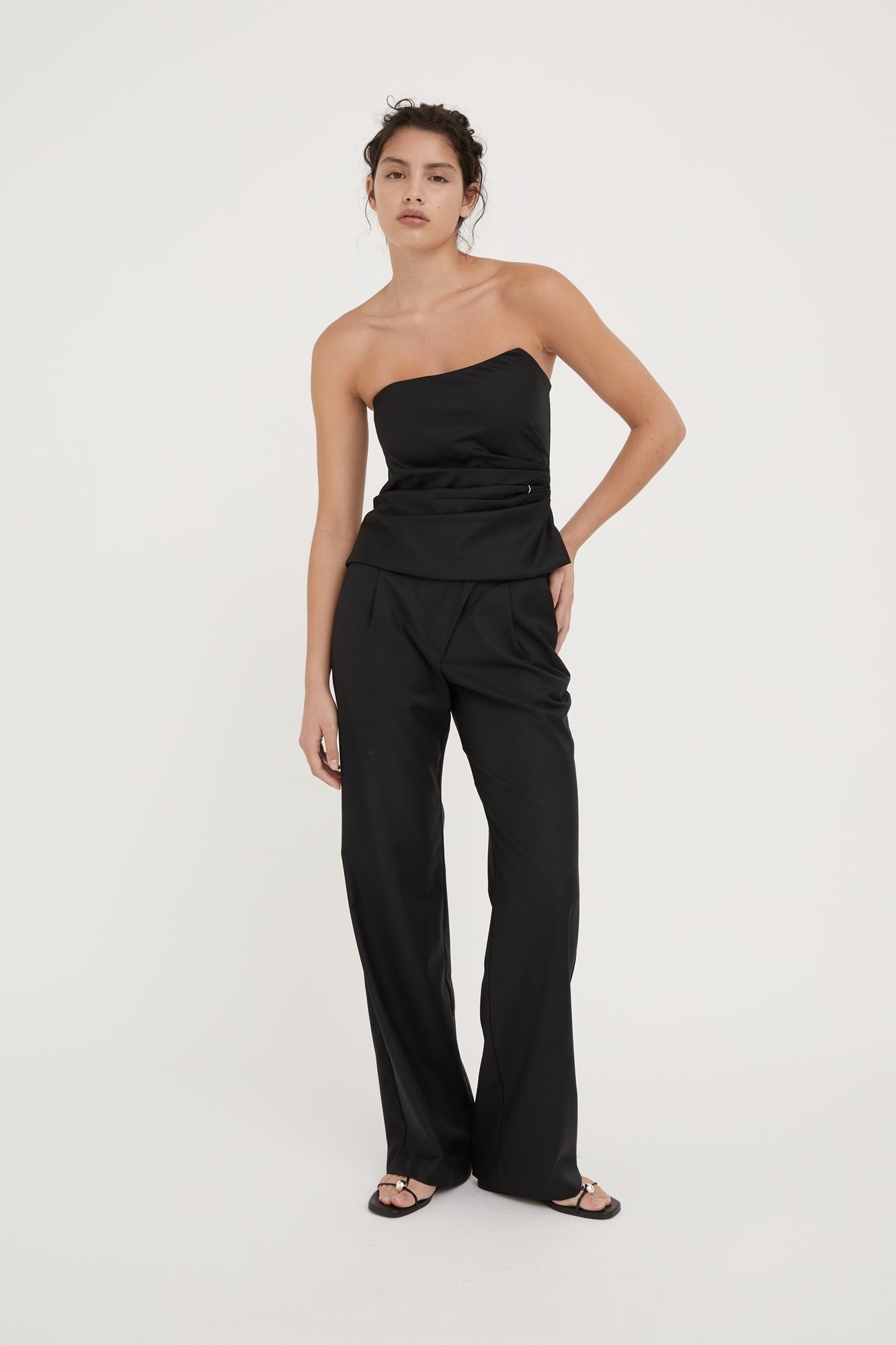Woman wearing a black strapless jumpsuit on a white background